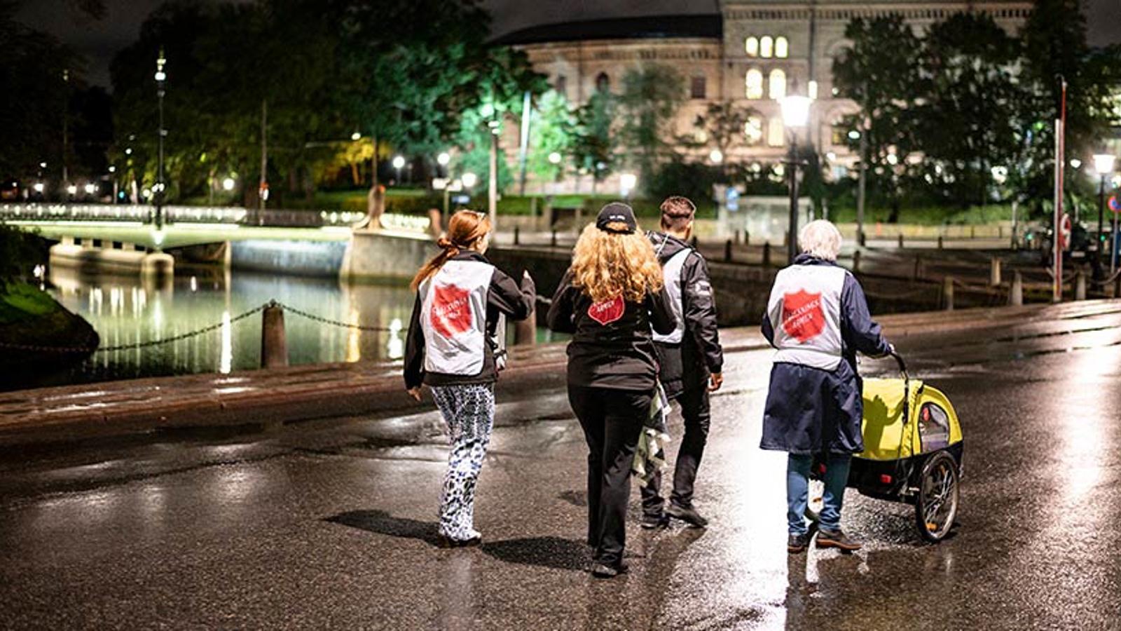 Fyra personer från Frälsningsarmén med ryggtavlorna mot kameran. De går tillsammans på Rosenlundsgatan.
