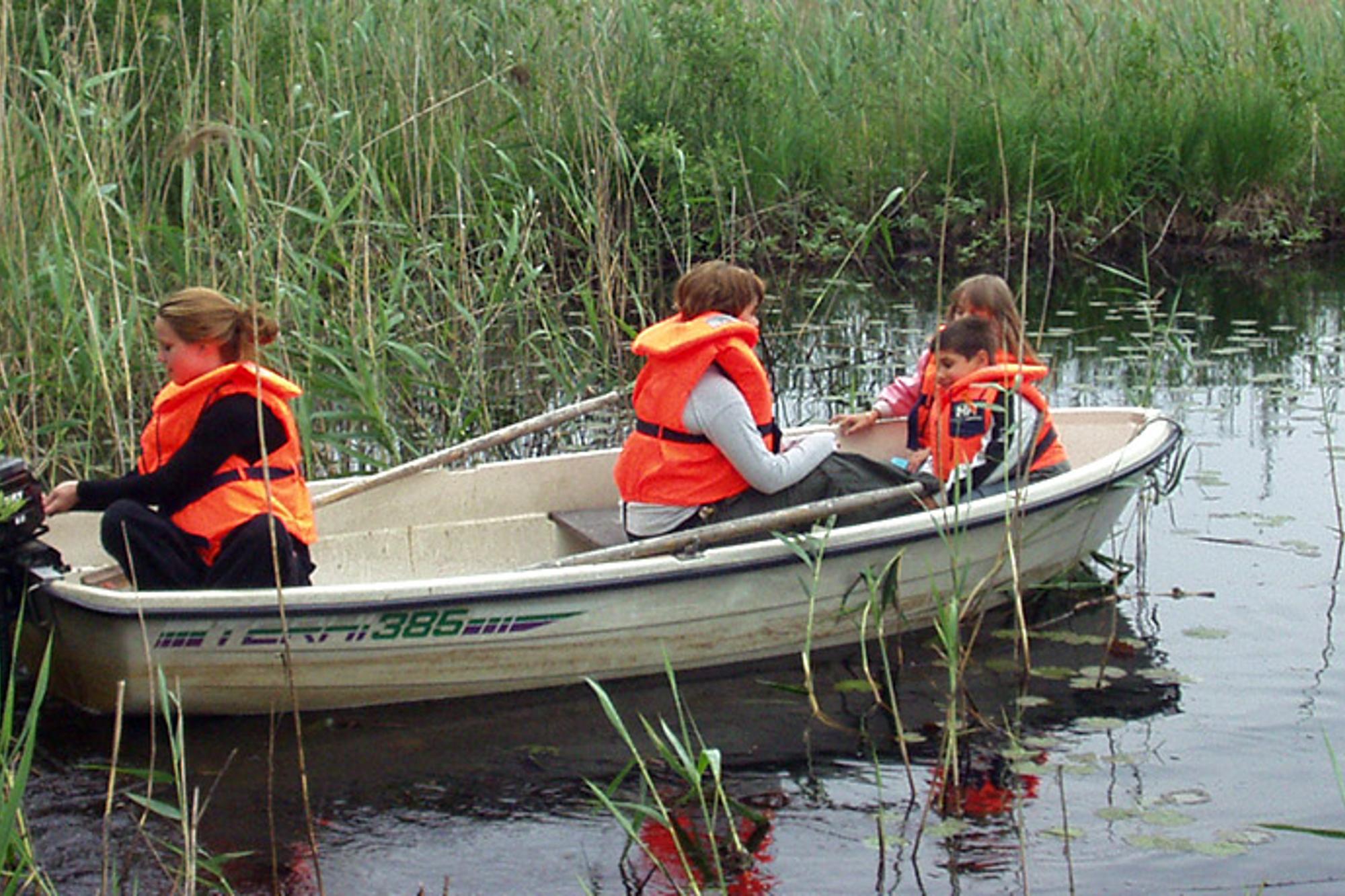 Två vuxna och två barn med flytvästar som sitter i en båt. 