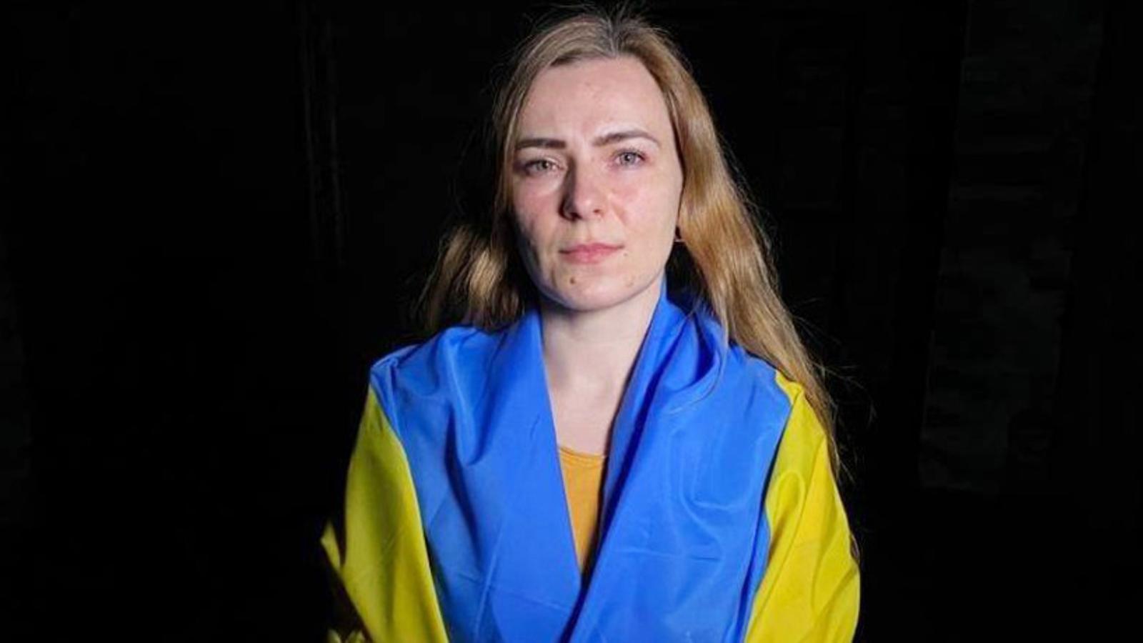Porträttbild av en kvinna, Tanya, som har den Ukrainska flaggan runt axlarna och tittar in i kameran.