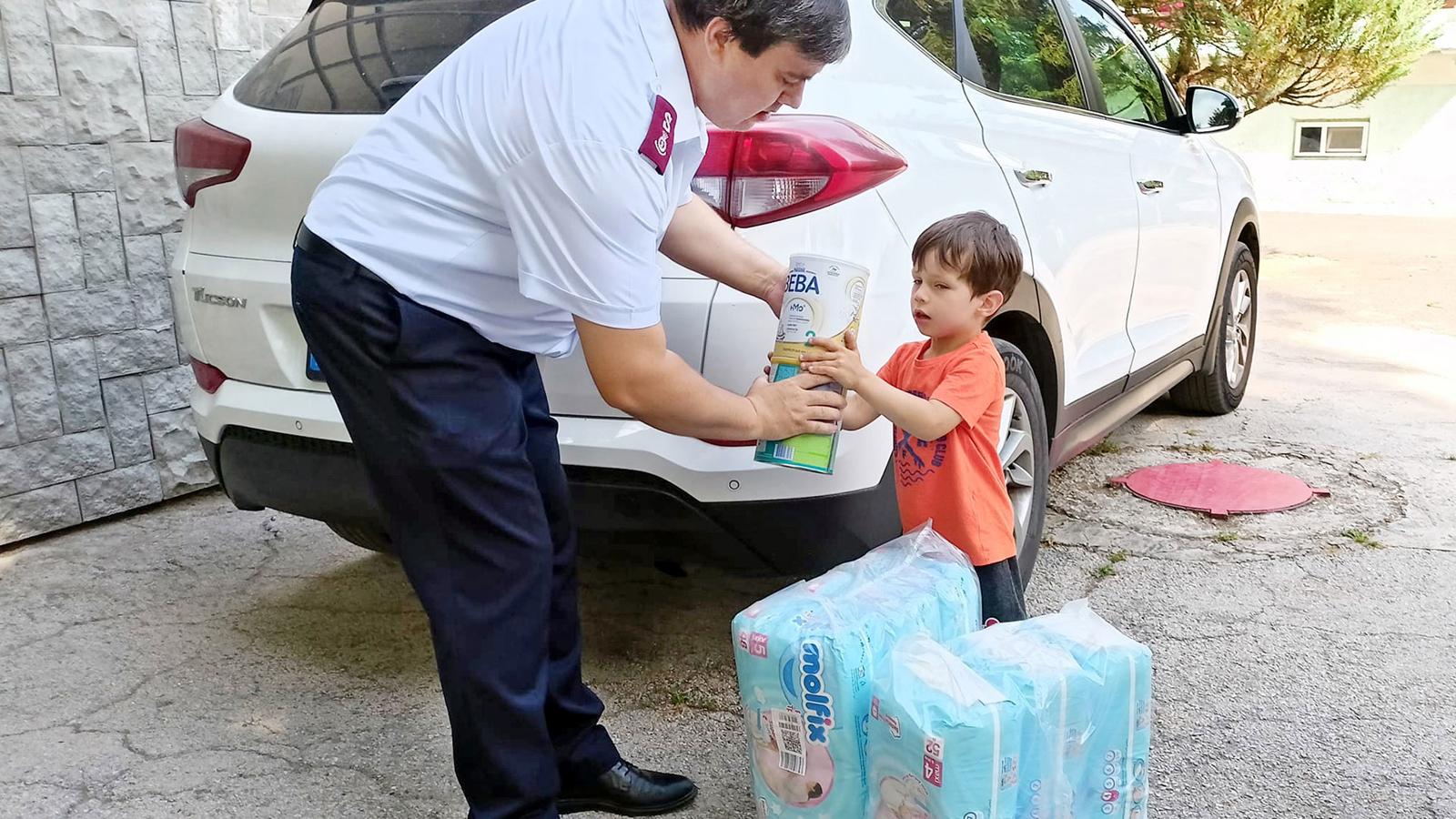 En man i Frälsningsarméns uniform ger ett paket med förnödenheter till ett litet barn. På marken står det fler paket.