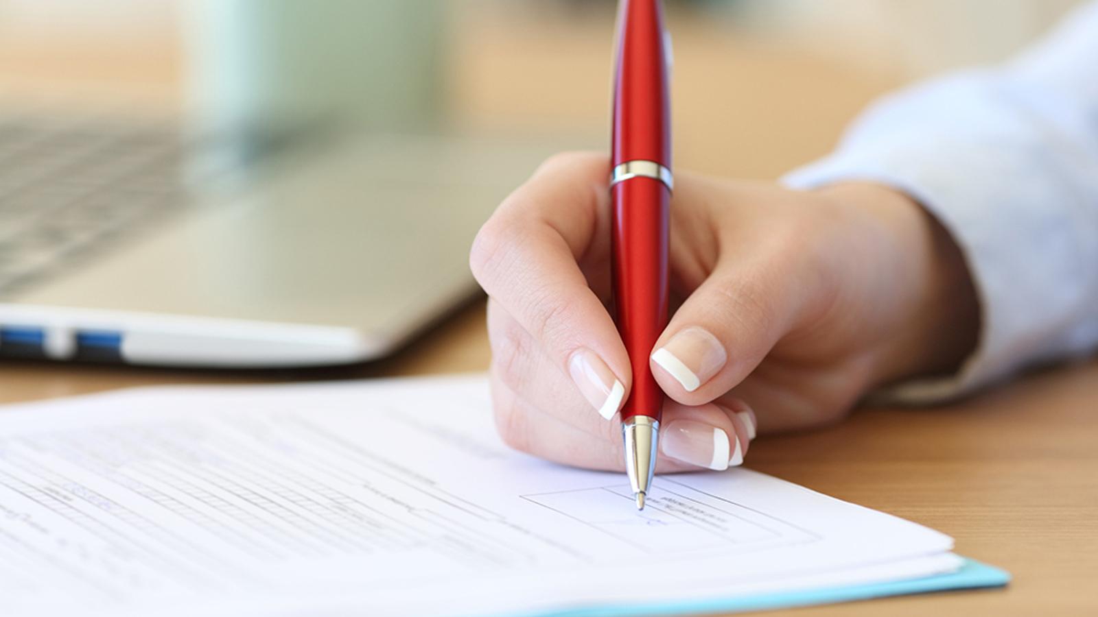 En person som håller i en penna och signerar ett dokument.
