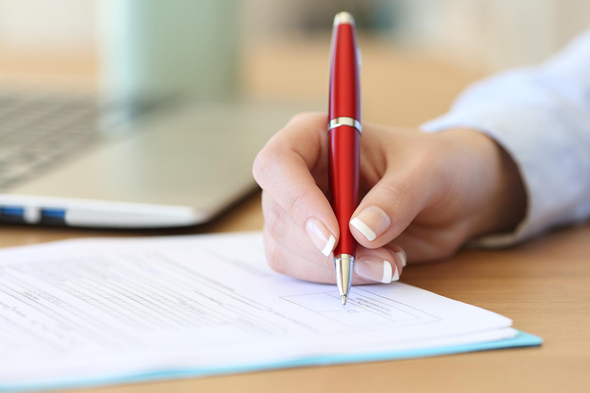 En person som håller i en penna och signerar ett dokument.