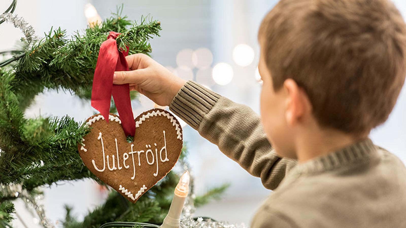 Pojke hänger pepparkakshjärta dekorerad "Julefröjd" i julgran