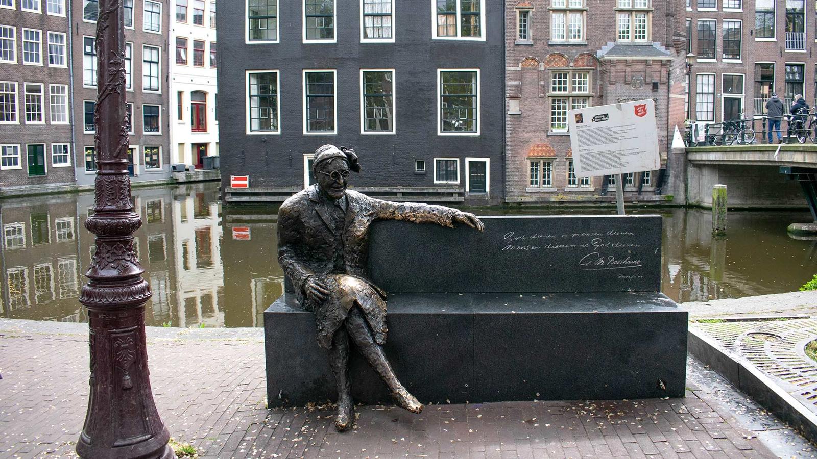 En staty, vid vattnet, utanför museet. Statyn föreställer en person som sitter på en bänk, och på bänken är en text ingraverad. Vid statyn står det en Frälsningsarmén-skylt med information om verket.