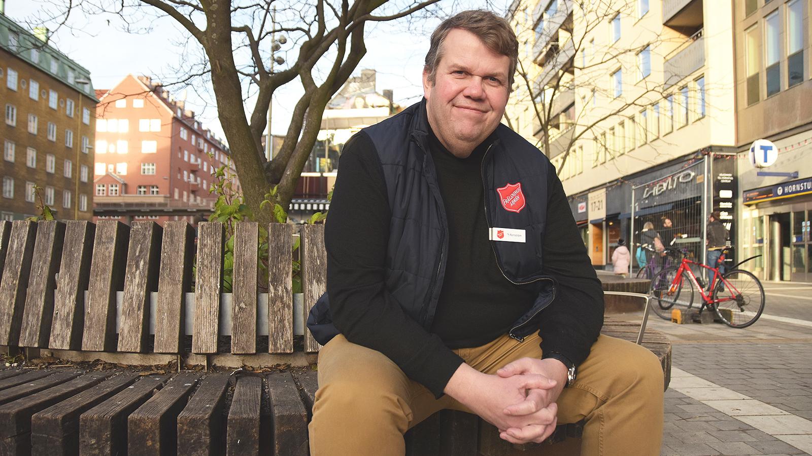 Per-Johan Fernström som sitter på en bänk. I bakgrunden syns ett torg med butiker och en tunnelbanestation.