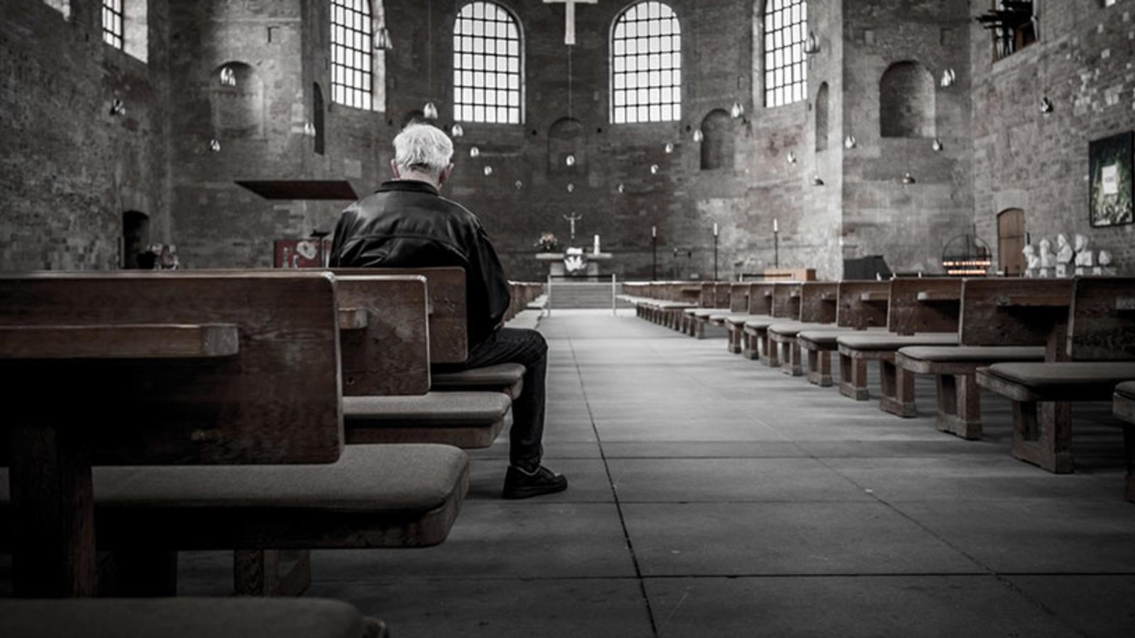 Ryggtavlan på en äldre man som sitter ensam i en kyrka.