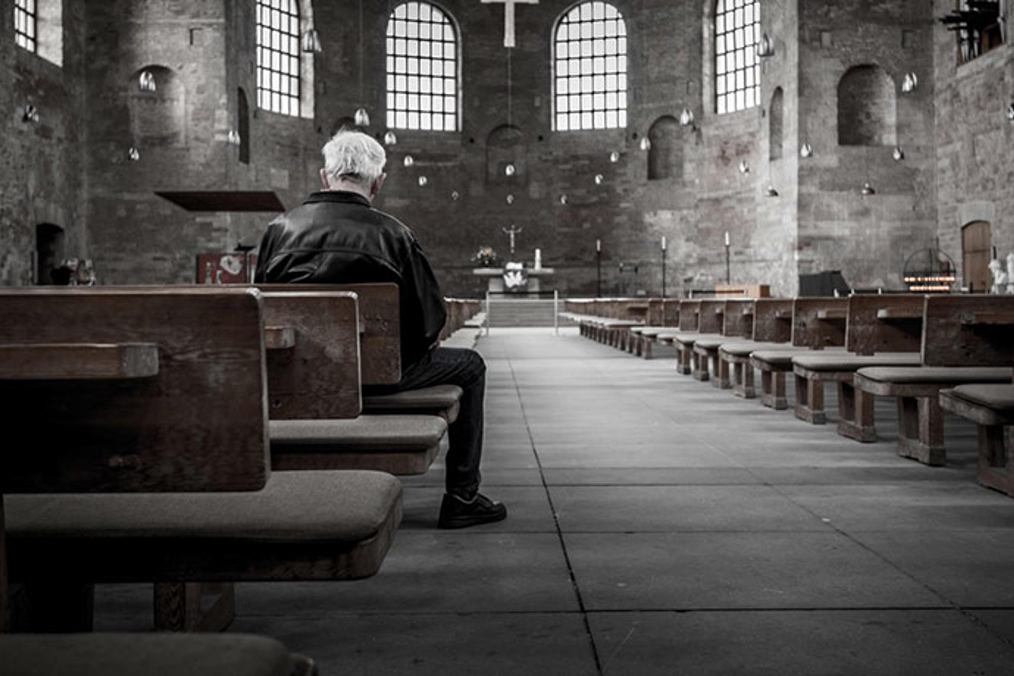 Ryggtavlan på en äldre man som sitter ensam i en kyrka.