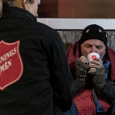 Frälsningsarmén anställd ger kopp med varmt kaffe och filt till en hemlös man på gatan.