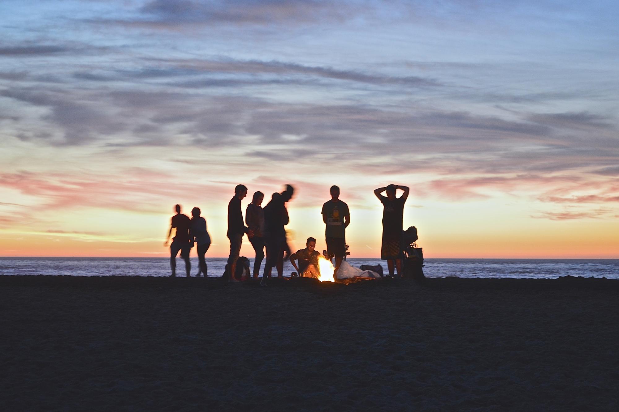 Ett gäng personer runt en brasa på en strand.