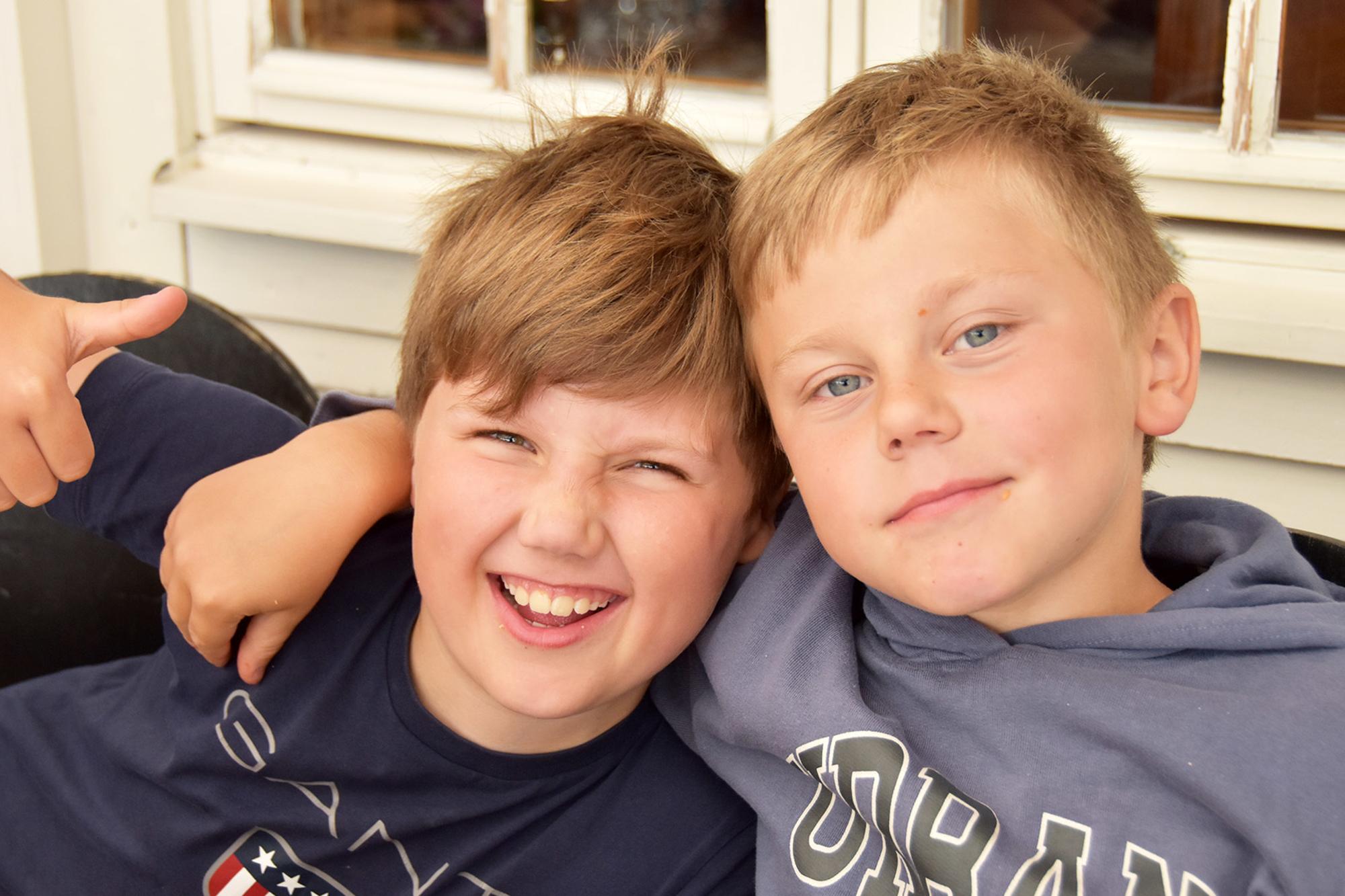 Två 10-åriga pojkar med armarna om varndras axlar tittar glatt in i kameran och gör tummen upp.