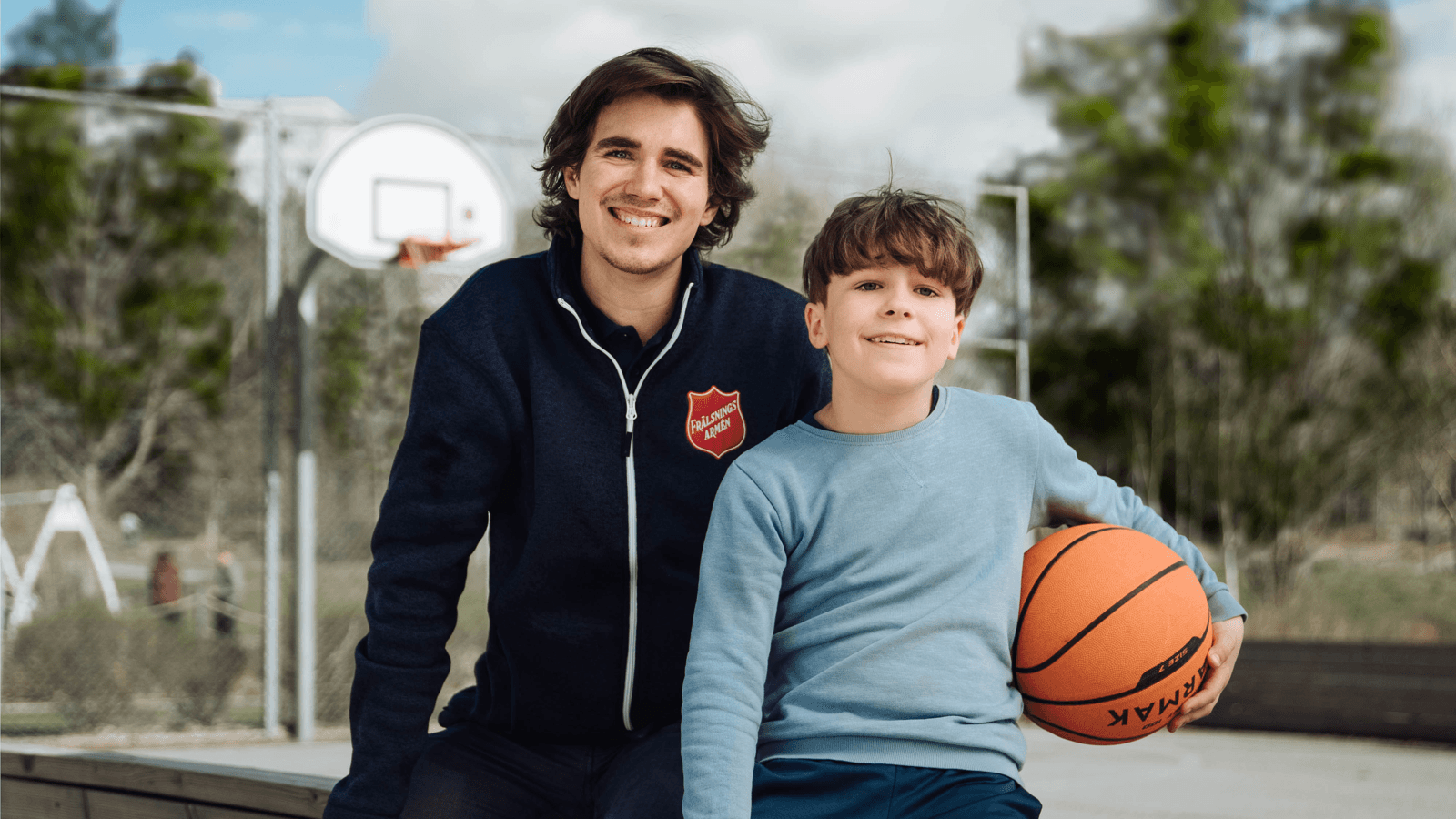 En pojke med en basketboll tillsammans med en av Frälsningsarméns personal.