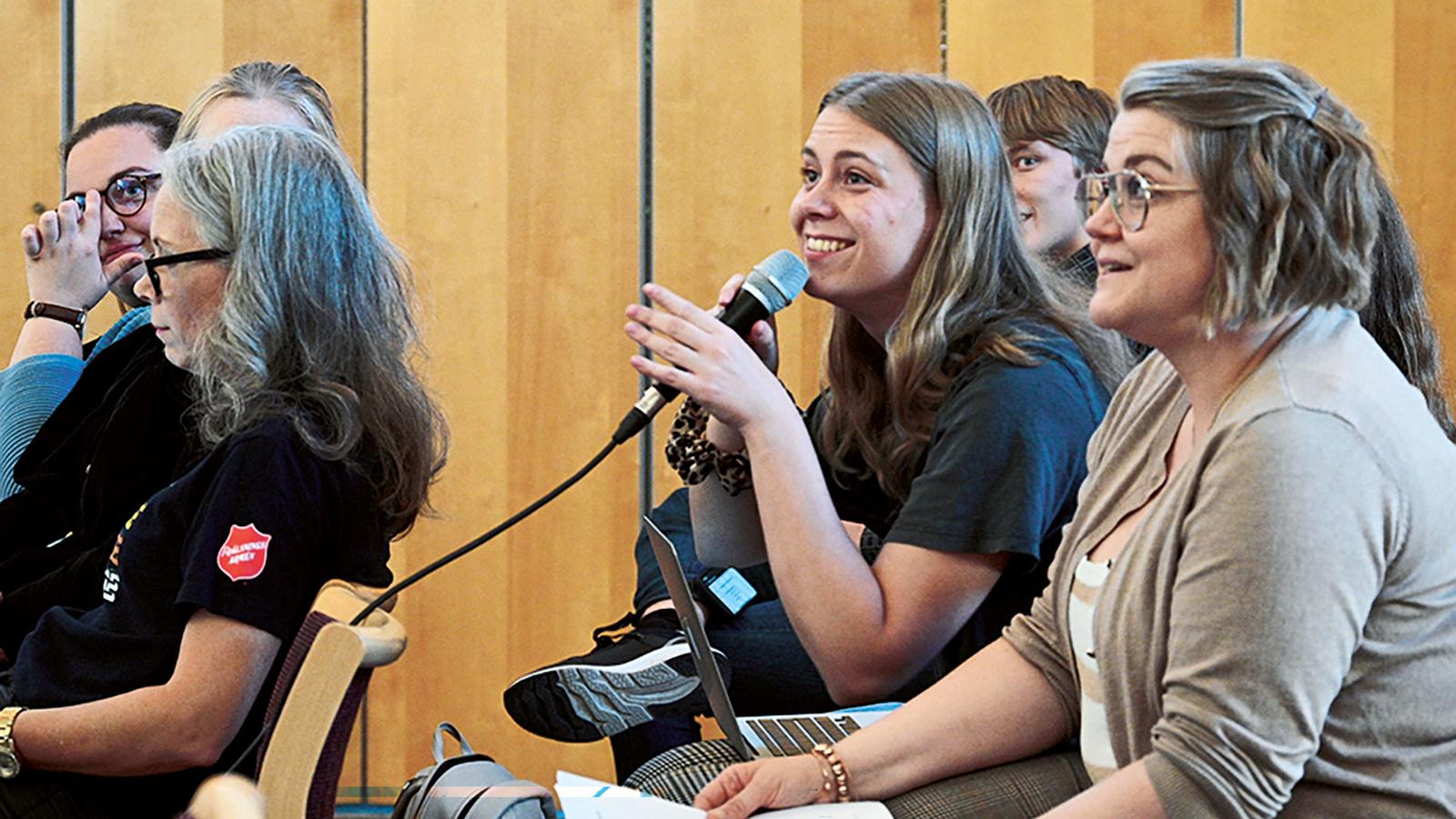 Ungdomar vid ett riksmöte inom Frälsningsarmén. En ung kvinna håller i en mikrofon och ler.