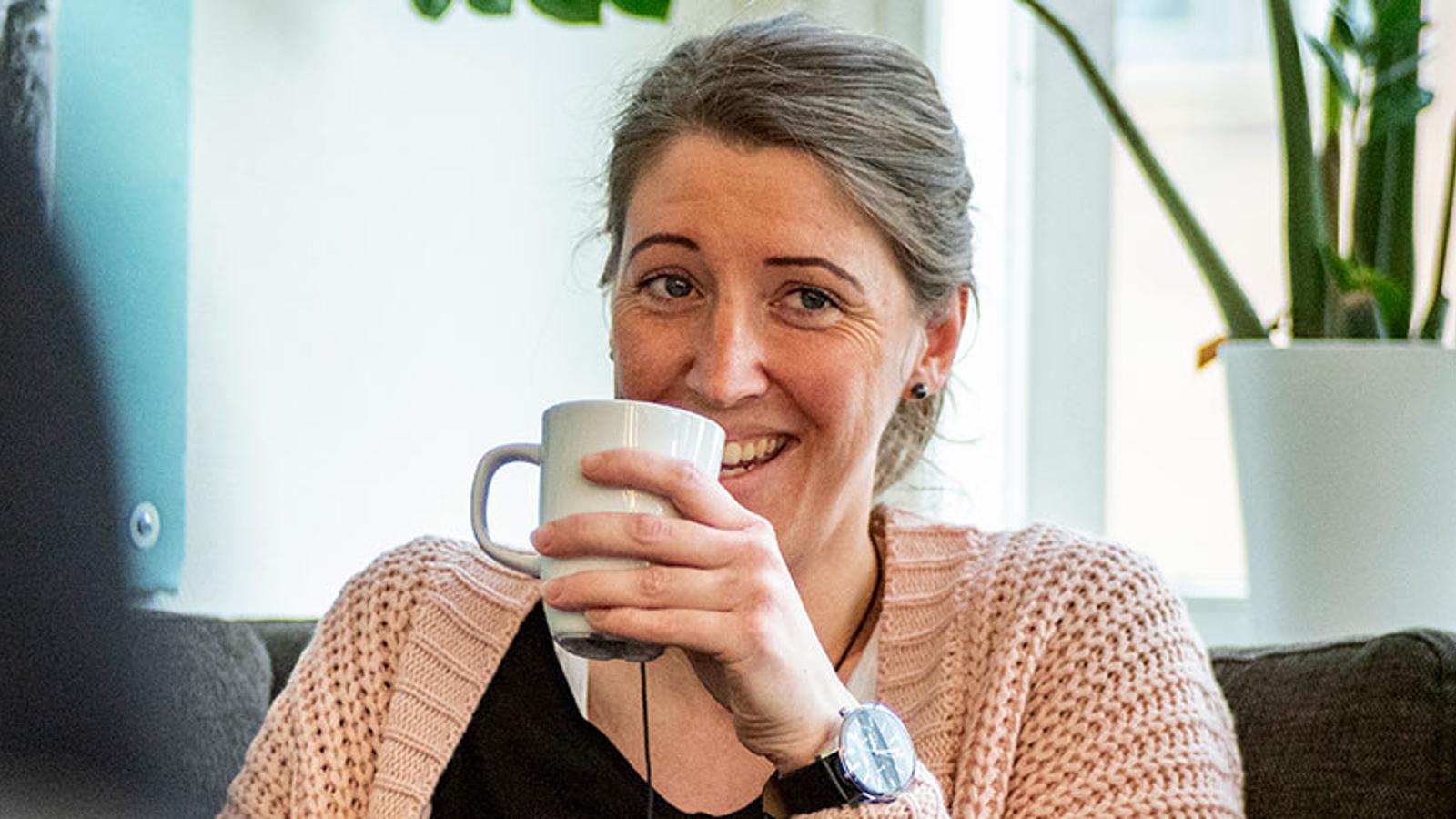 En glad kvinna som tittar förbi kameran och håller i en kaffemugg.