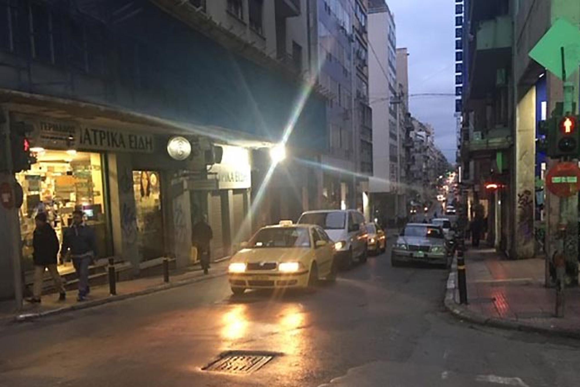 Det tuffa kvarteret Omonia i Aten, där bilar kommer åkandes på en bilväg. Till vänster och höger om bilvägen går det människor på gatorna.