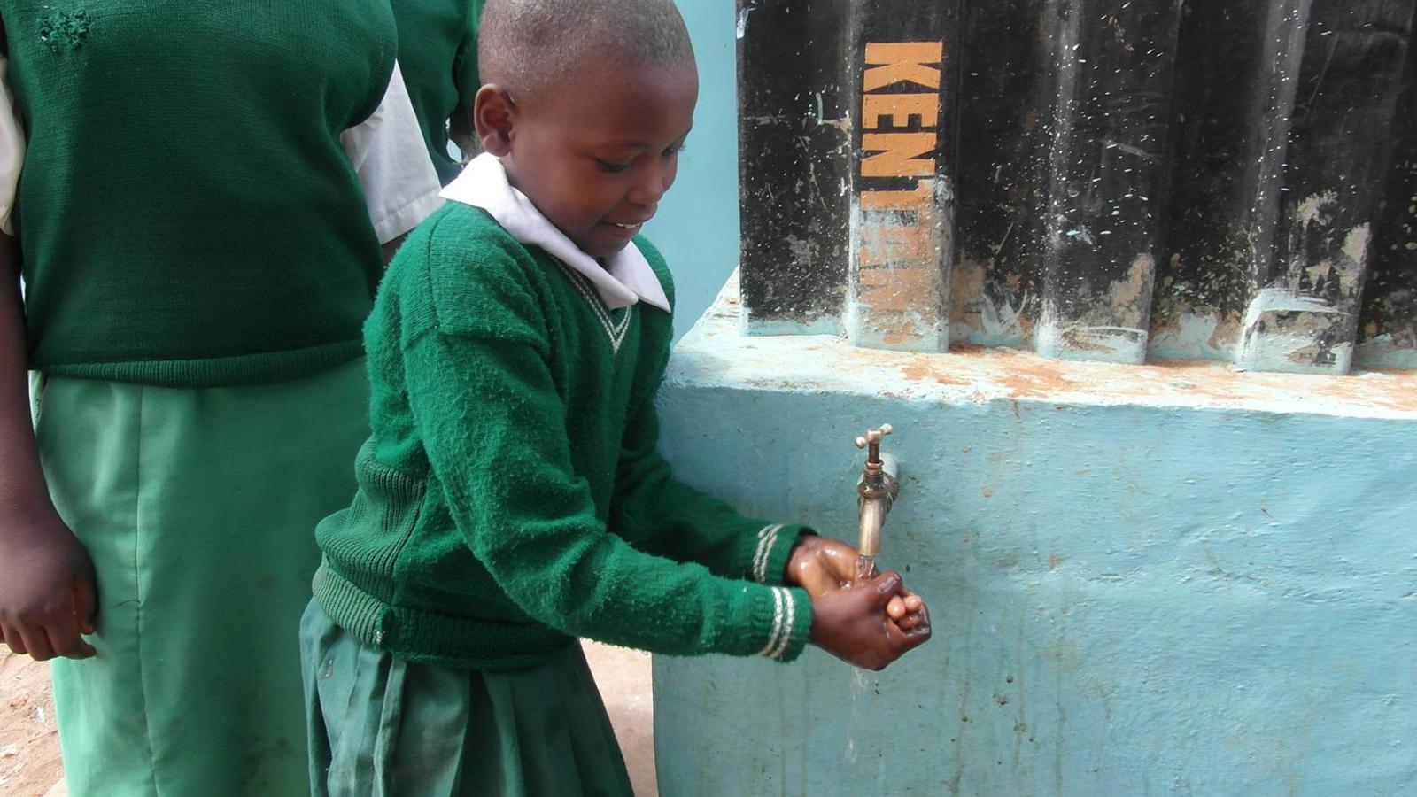 En glad flicka i skoluniform som står och tvättar händerna.