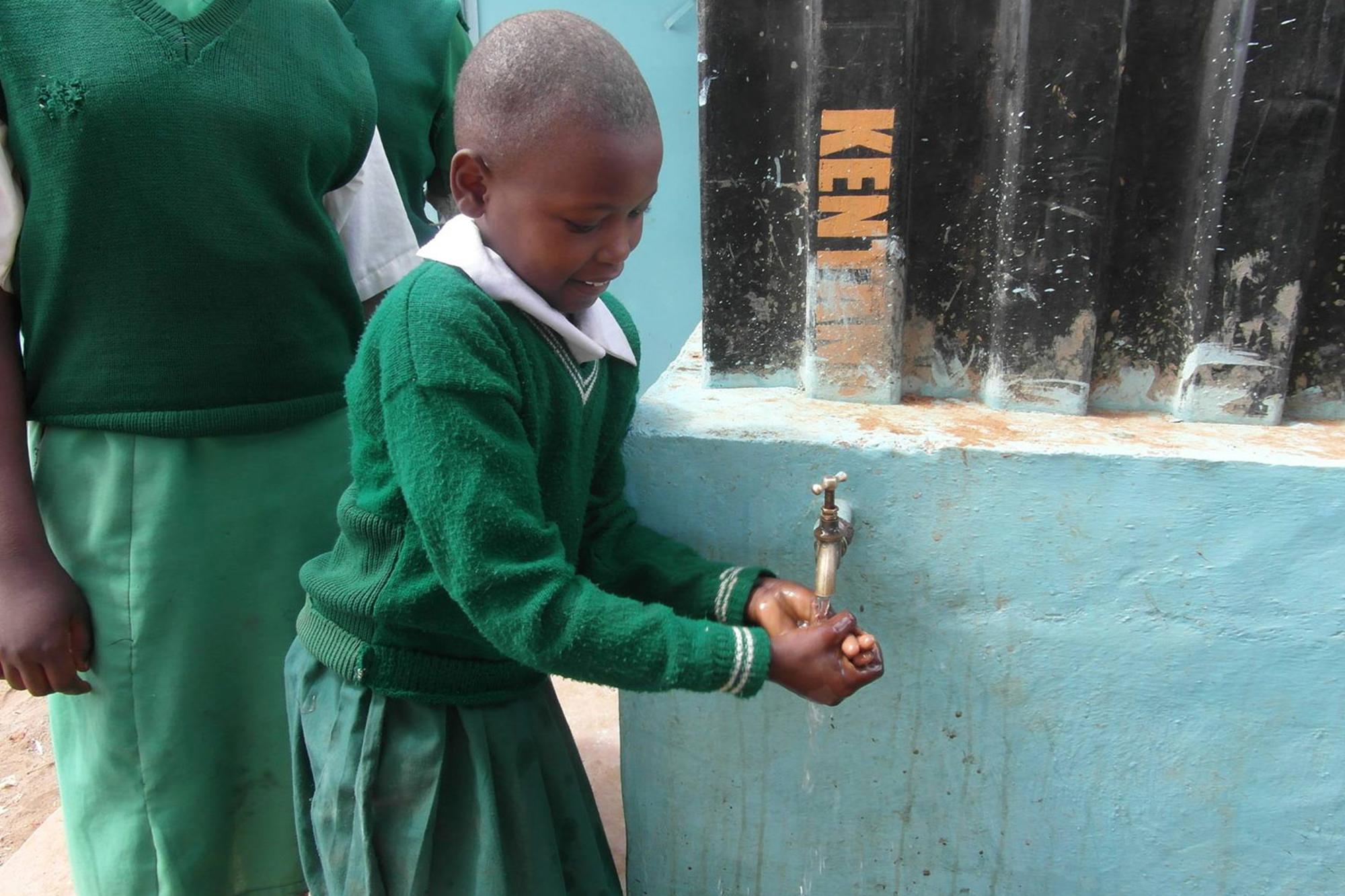 En glad flicka i skoluniform som står och tvättar händerna.