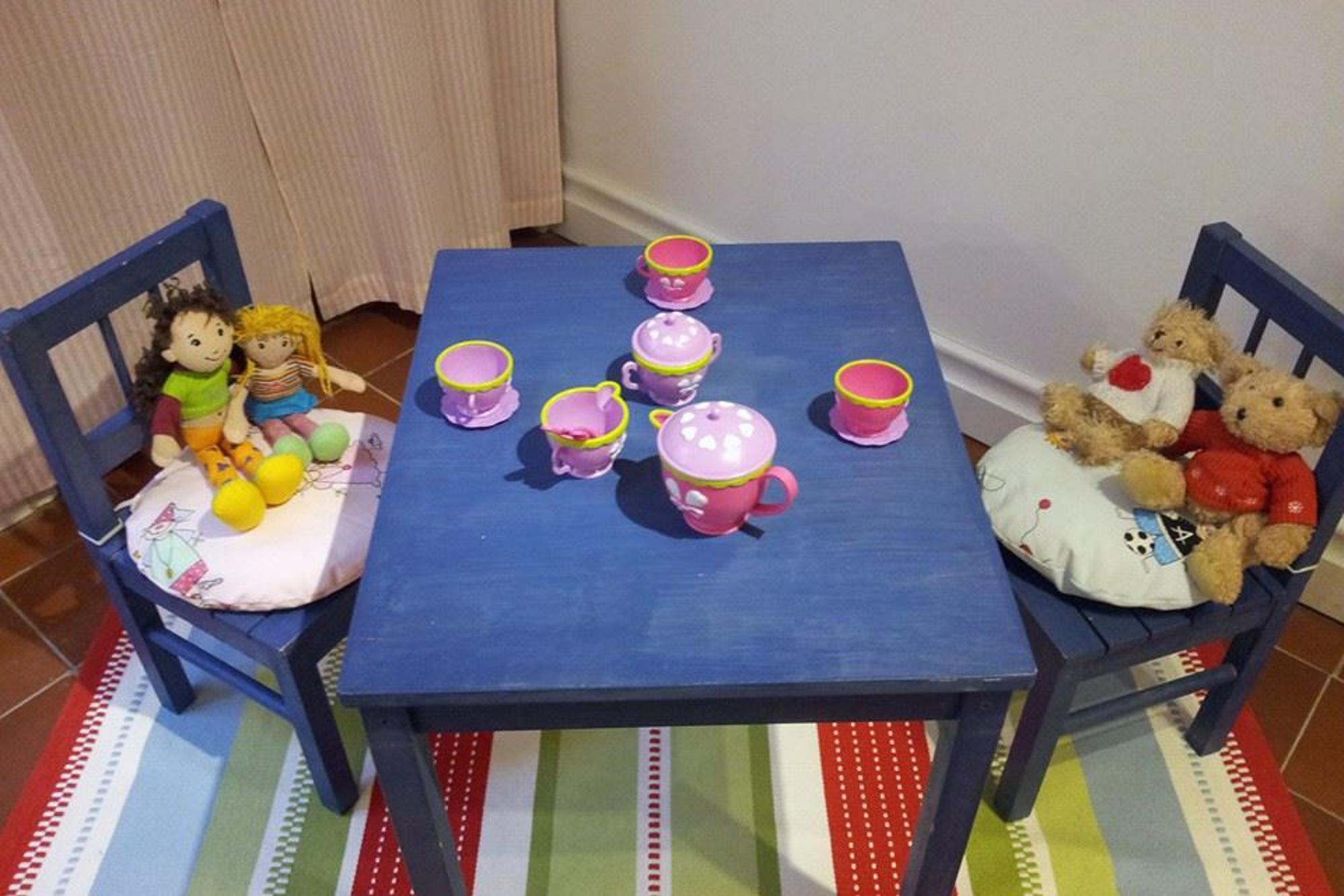 Ett litet bord med några leksakskoppar och en kanna. Vid bordet står det två stolar med gosedjur på.