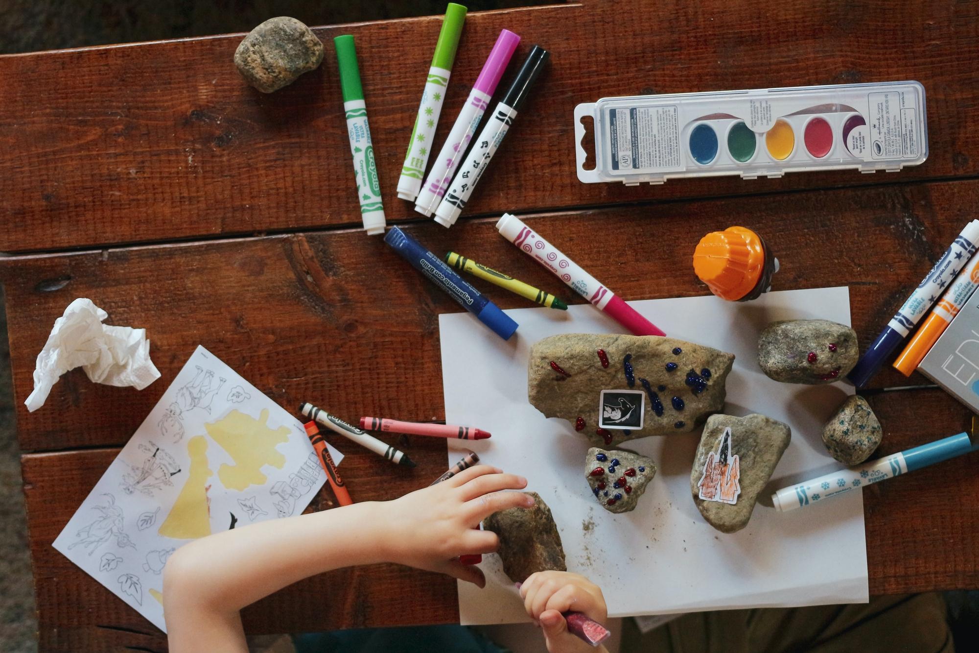 Ett barn som sitter vid ett bord och pysslar. På bordet ligger det kritor, tuschpennor, målarfärg och glitter.