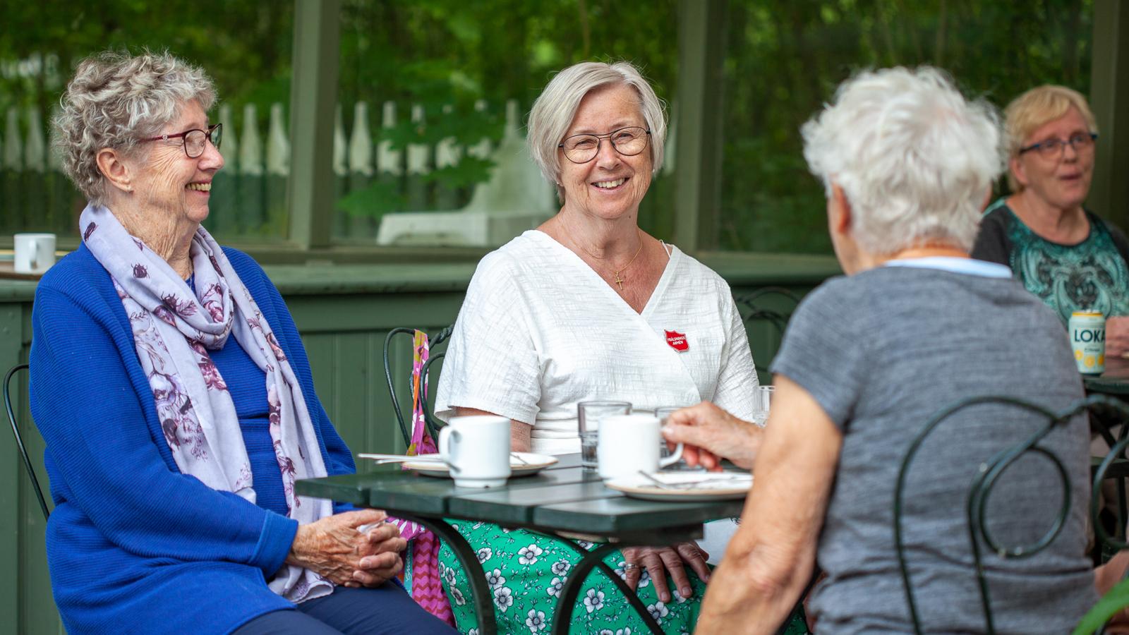 Tre glada äldre damer som sitter och fikar.
