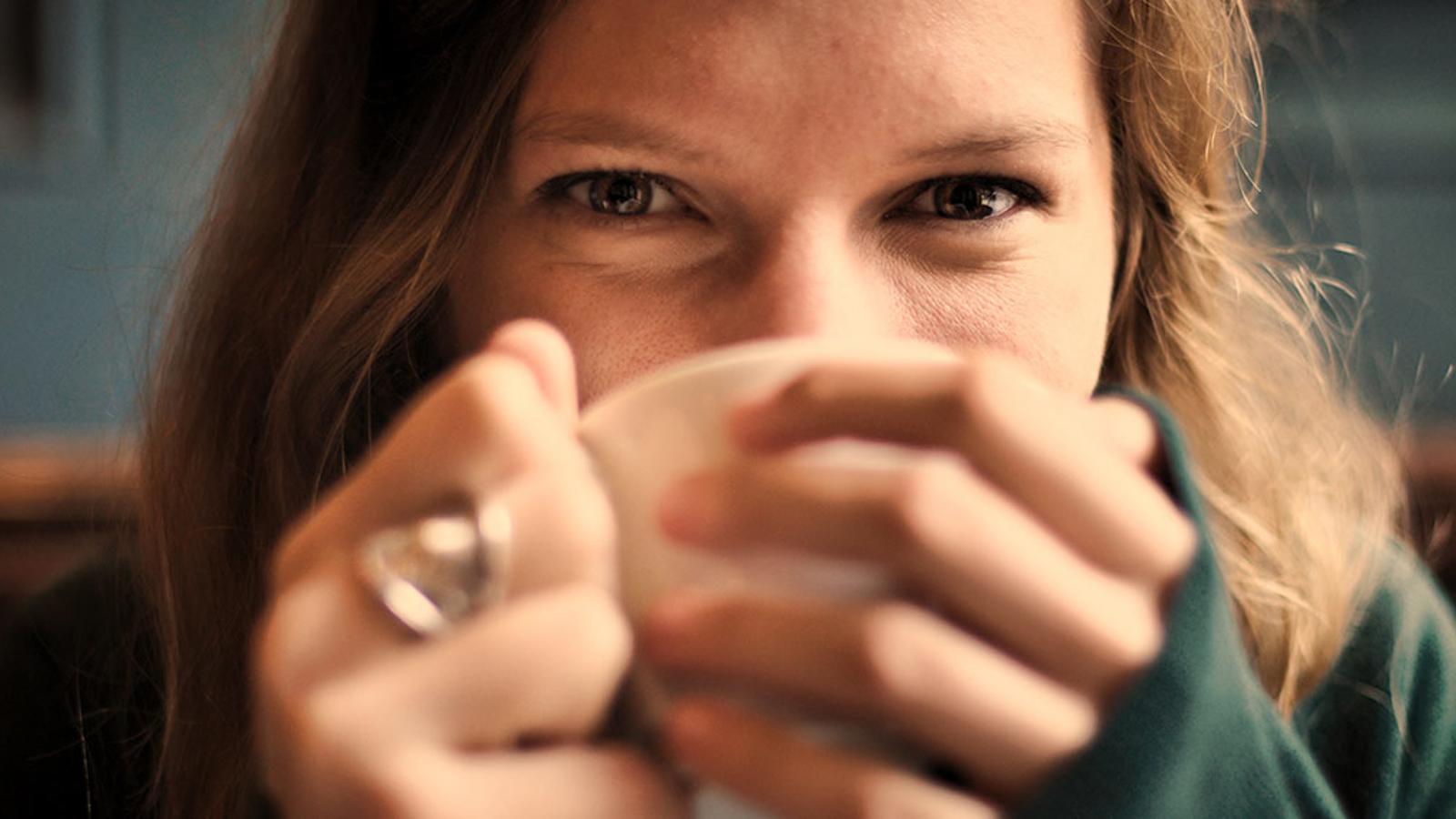 En kvinna som håller en kaffemugg för sin näsa och mun.