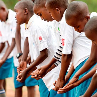 Unga pojkar i Kenya står på rad i skoluniform med Frälsningsarméns sköld på ärmen och tvättar händerna. 