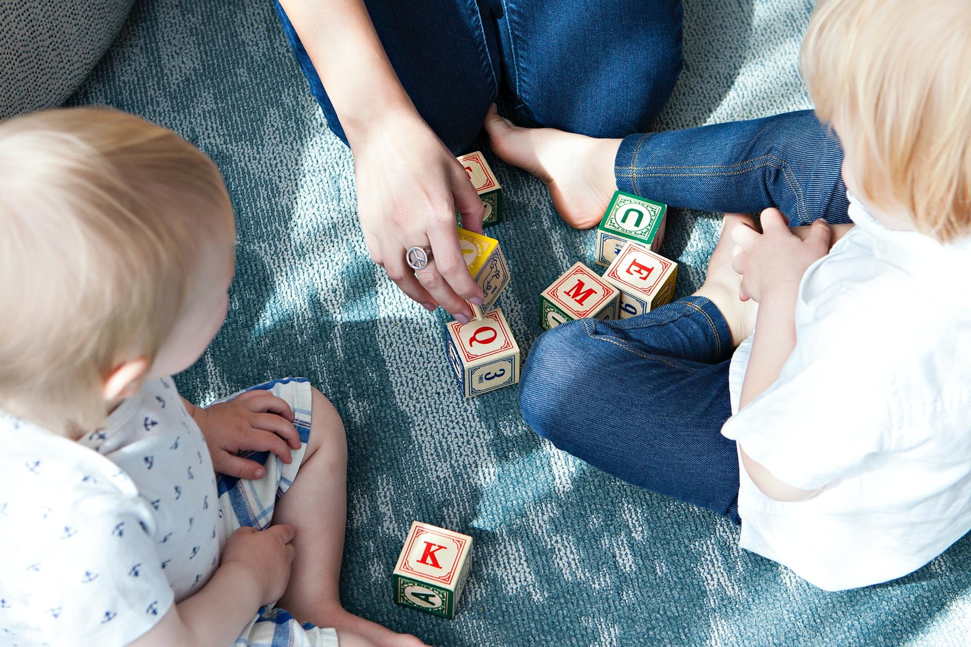 Två barn och en vuxen som sitter på golvet och leker med klossar.
