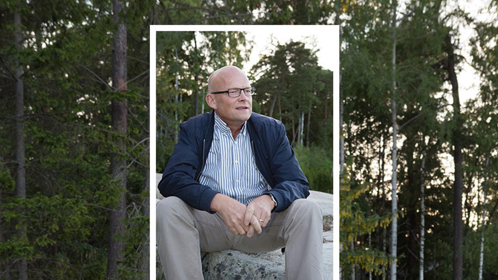 Porträttbild av Peter Ågren som sitter på en sten och tittar till höger om kameran. Bakgrunden består av träd i en skog.