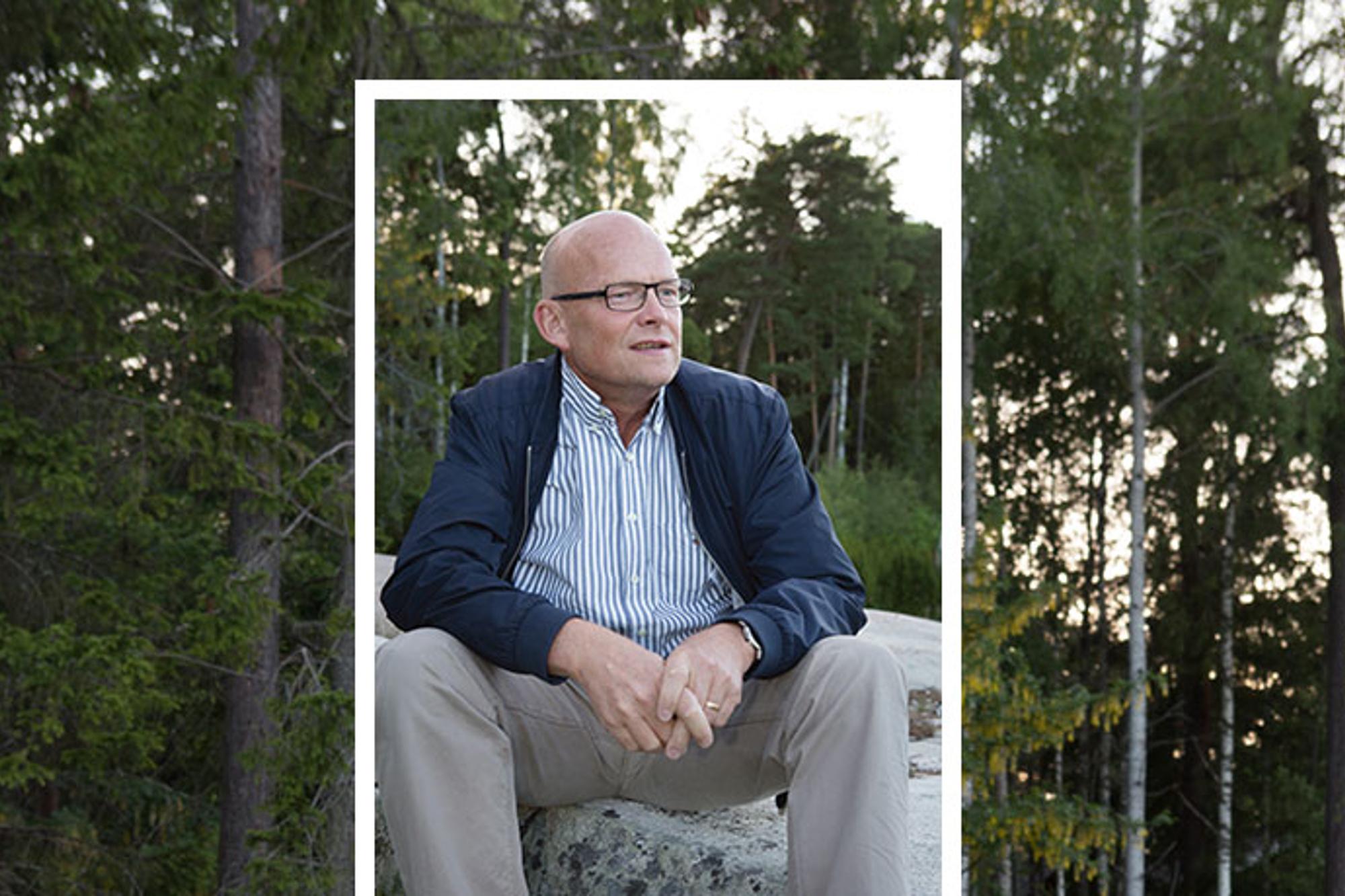 Porträttbild av Peter Ågren som sitter på en sten och tittar till höger om kameran. Bakgrunden består av träd i en skog.