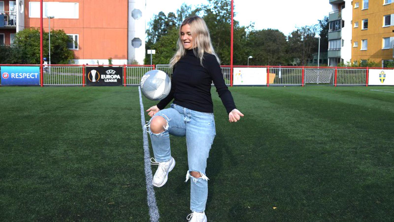 Julia Adolfsson på en fotbollsplan. Hon kickar en fotboll med ena knät.