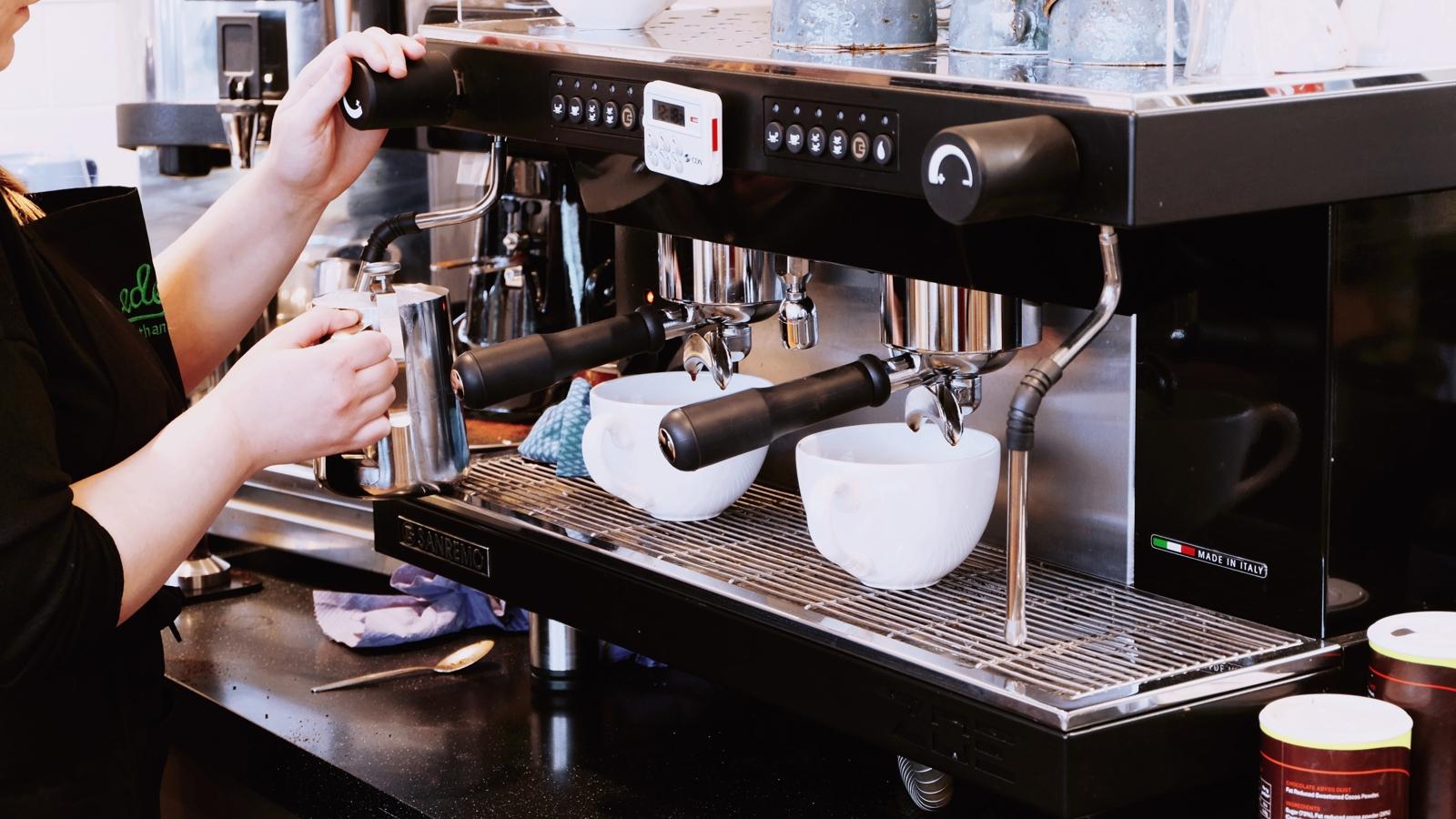 En barista som står och skummar mjölk vid en espressomaskin.