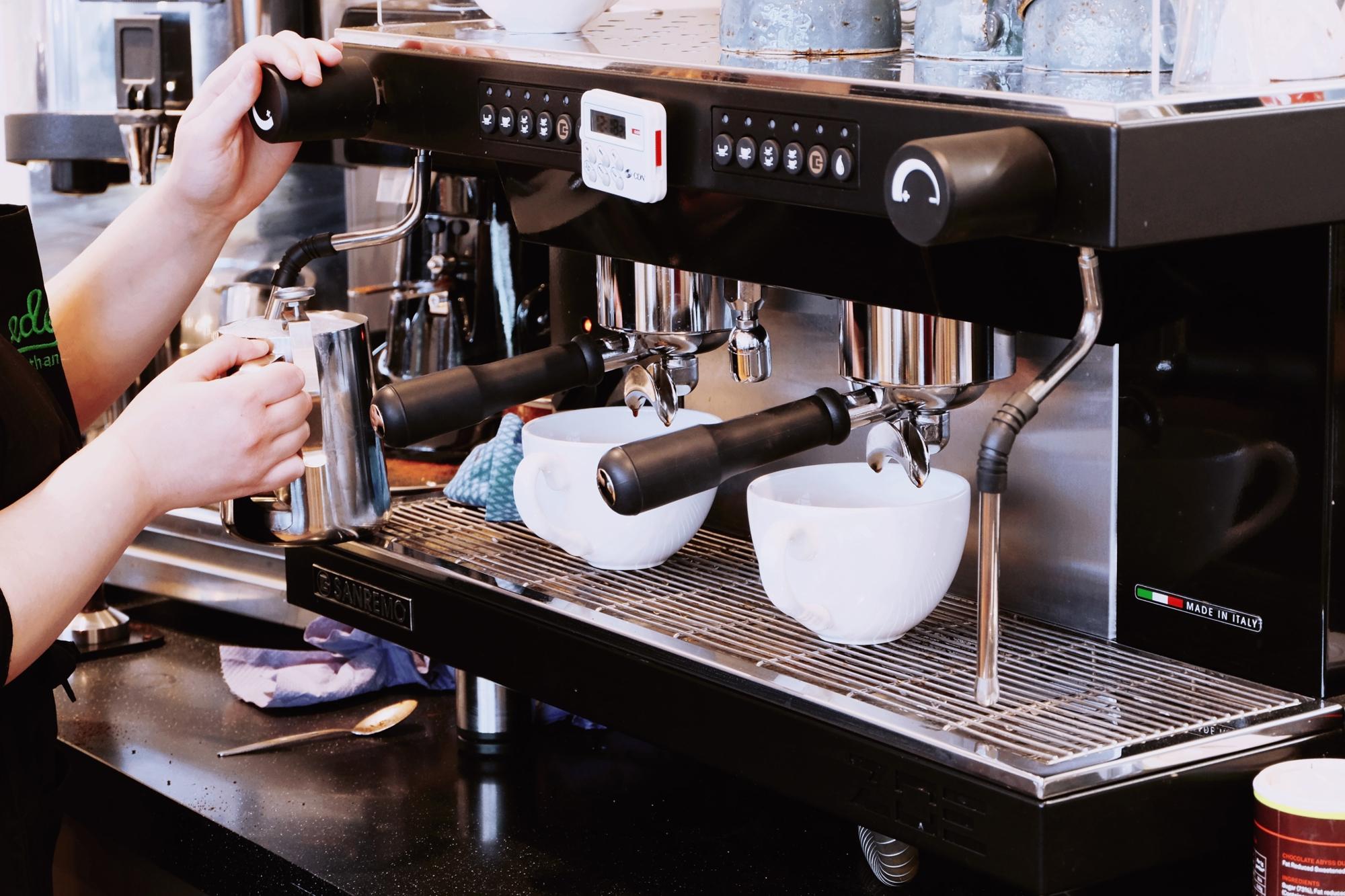 En barista som står och skummar mjölk vid en espressomaskin.