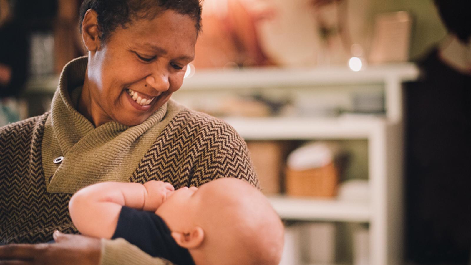 En glad kvinna som håller i ett spädbarn. Hon ler stort mot barnet.