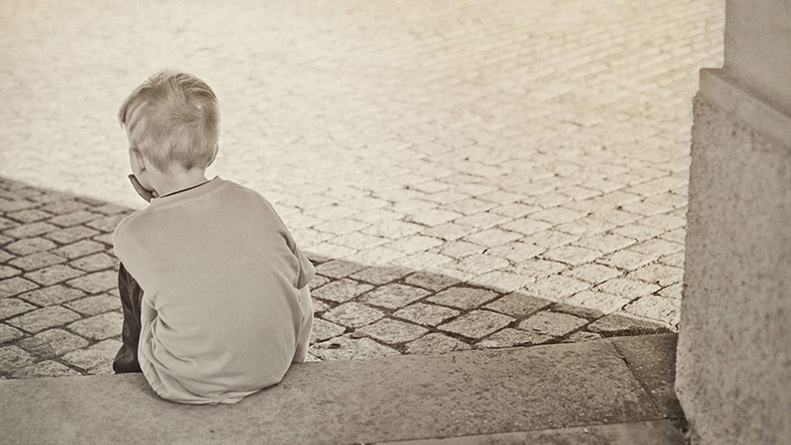 Ryggtavlan på en liten pojke som sitter ensam på en stentrappa.