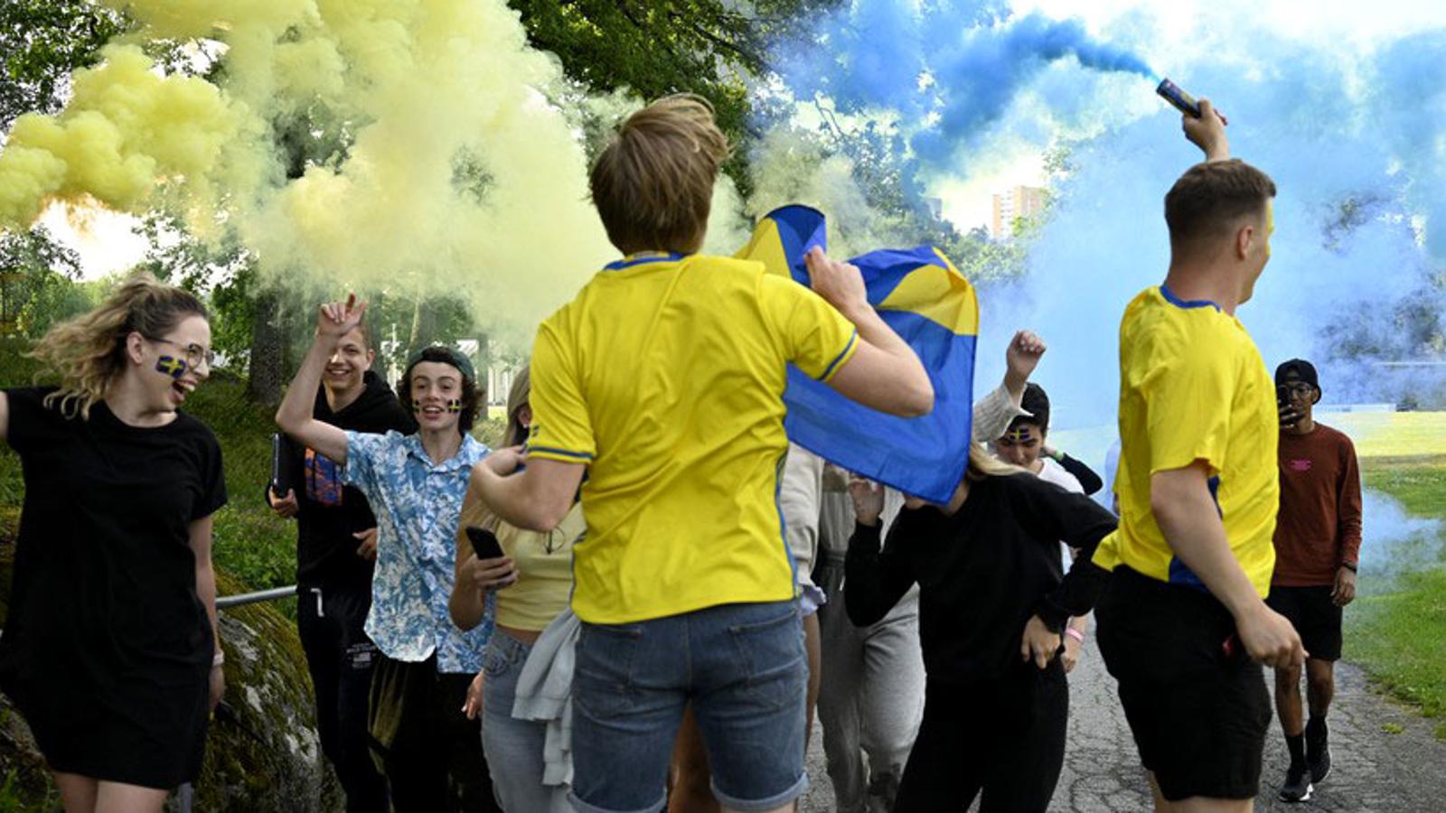 Glada konfirmander i blåa och gula kläder. De har Sverige-flaggor målade i ansiktet.