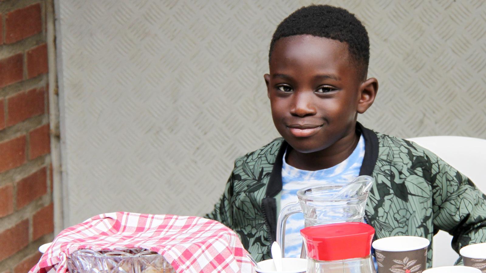 En liten pojke sitter bakom ett bord med bullar och saft att dela ut.