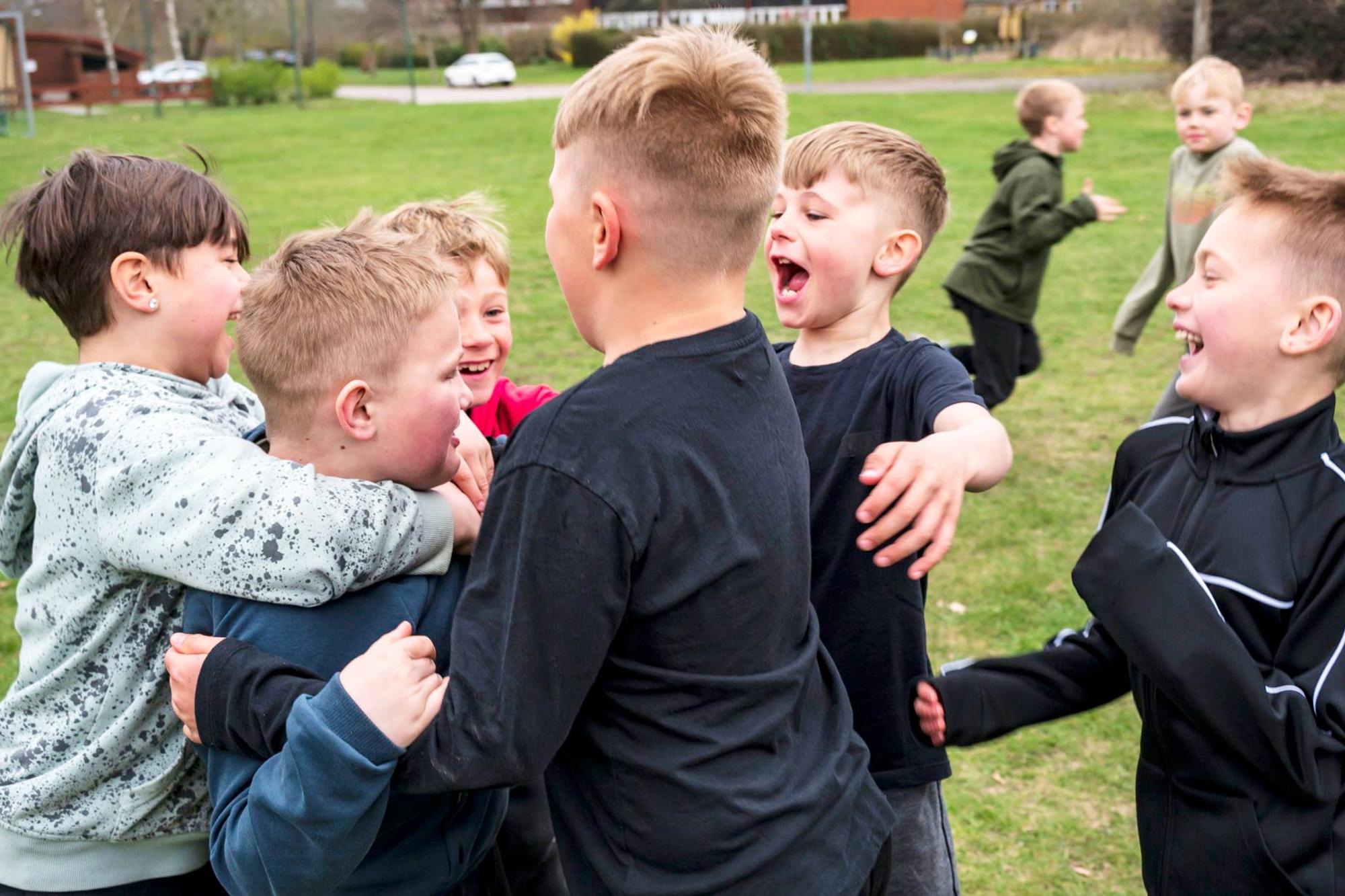 Ett gäng glada killar i 10-årsåldern kramar om varandra på fotbollsplanen.