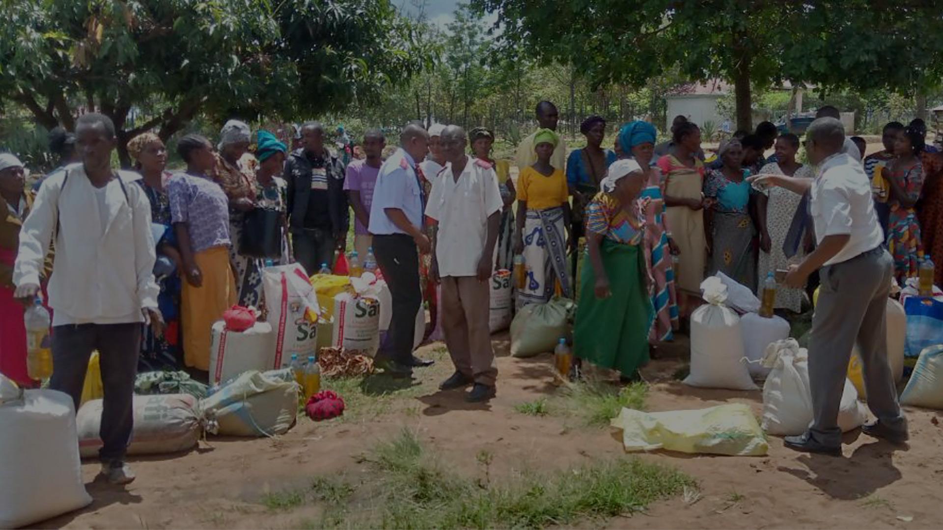 En folksamling i Serengeti där tre män med Frälsningsarméns uniform delar ut mat från säckar som står på marken.