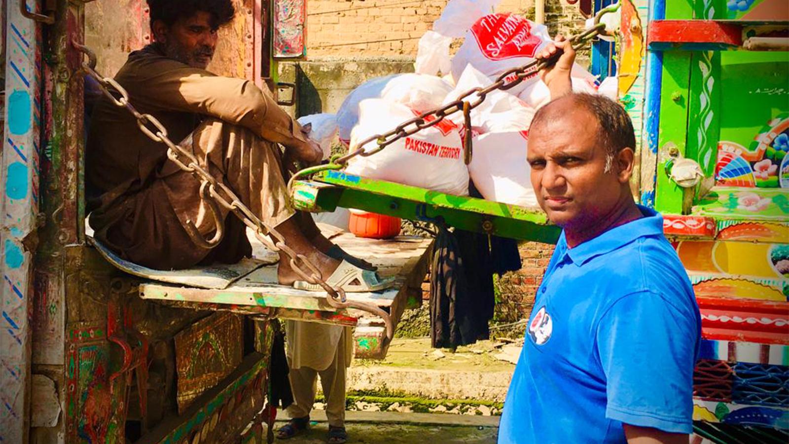 Två män i Pakistan som står vid påsar från Frälsningsarmén. I påsarna ligger det förnödenheter i form av bland annat mat, hygienartiklar och filtar.