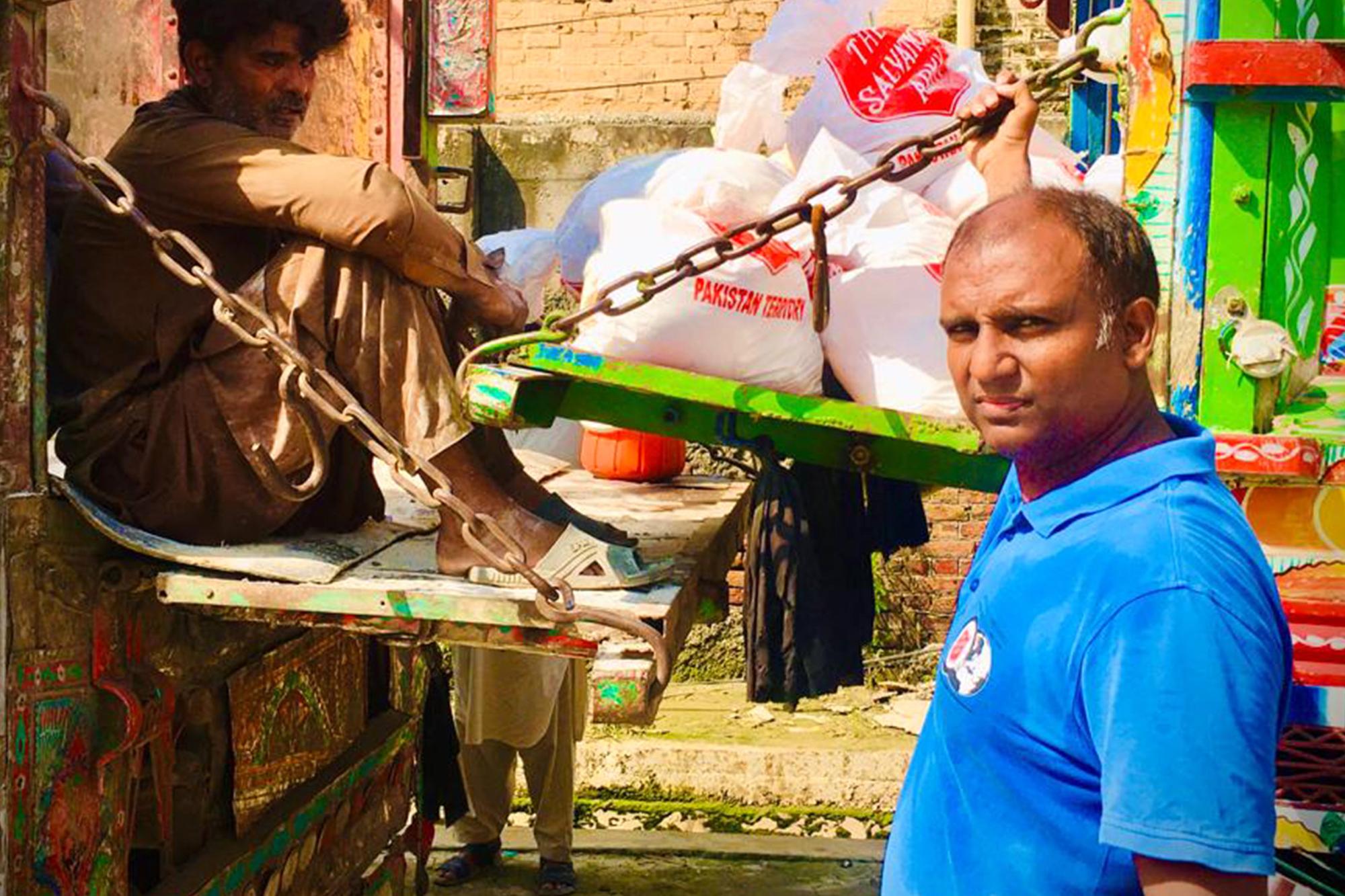 Två män i Pakistan som står vid påsar från Frälsningsarmén. I påsarna ligger det förnödenheter i form av bland annat mat, hygienartiklar och filtar.