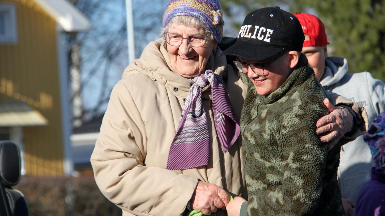 En äldre kvinna och en pojke i 10-årsåldern håller leende om varandra.