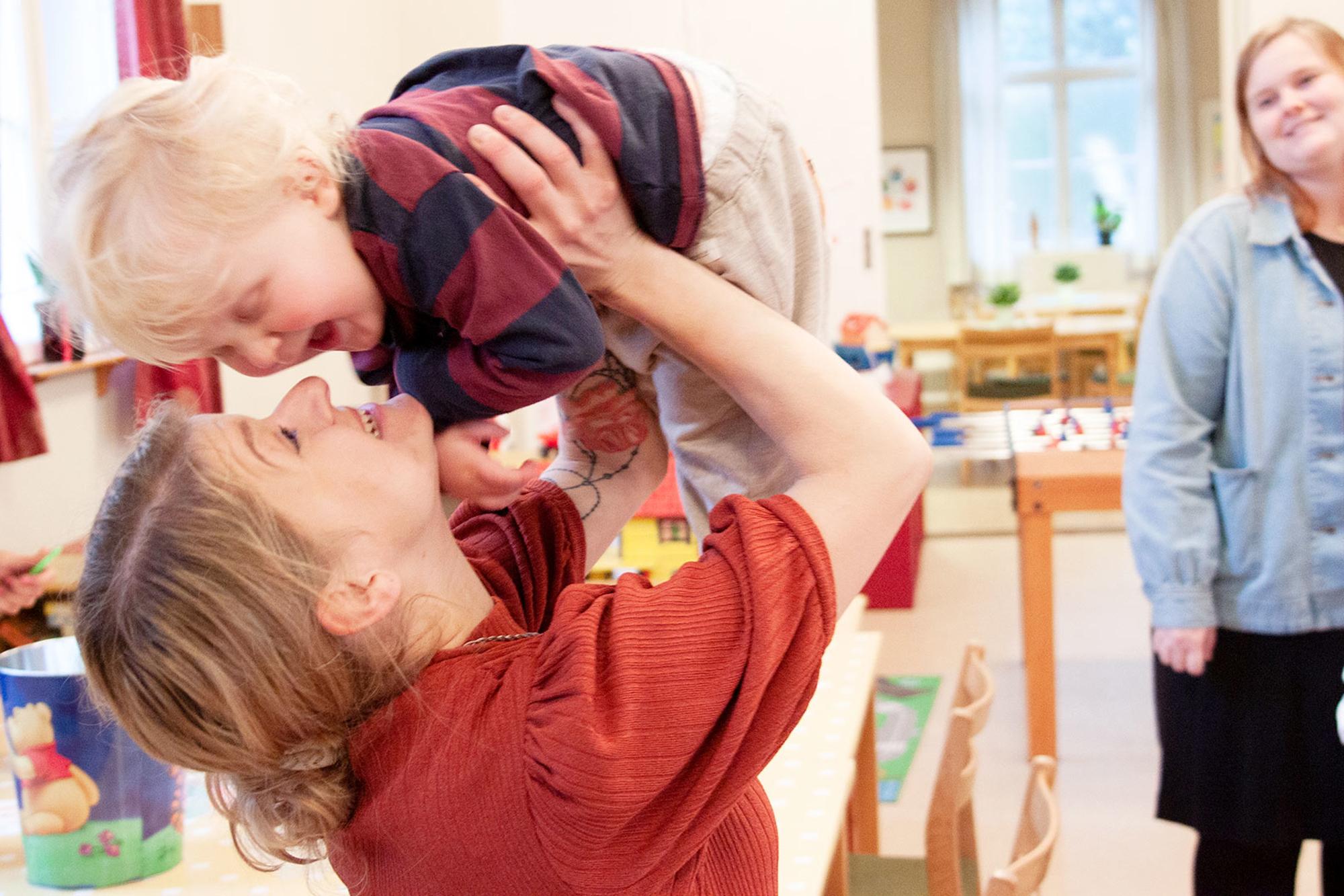 En mamma hissar skrattande sin leende lille son upp i luften inne på Frälsningsarmén i Eksjö. Runt omkring dem står Pernilla och Lina och tittar leende på.