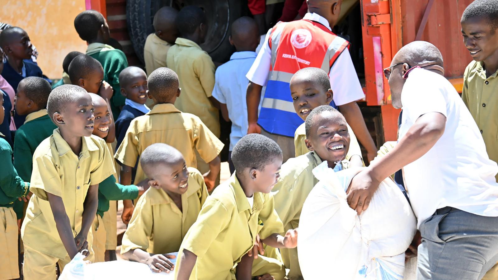 Ett gäng unga glada kenyanska pojkar hjälper till att ta emot säckar med majsmjöl från Frälsningsarméns personal.