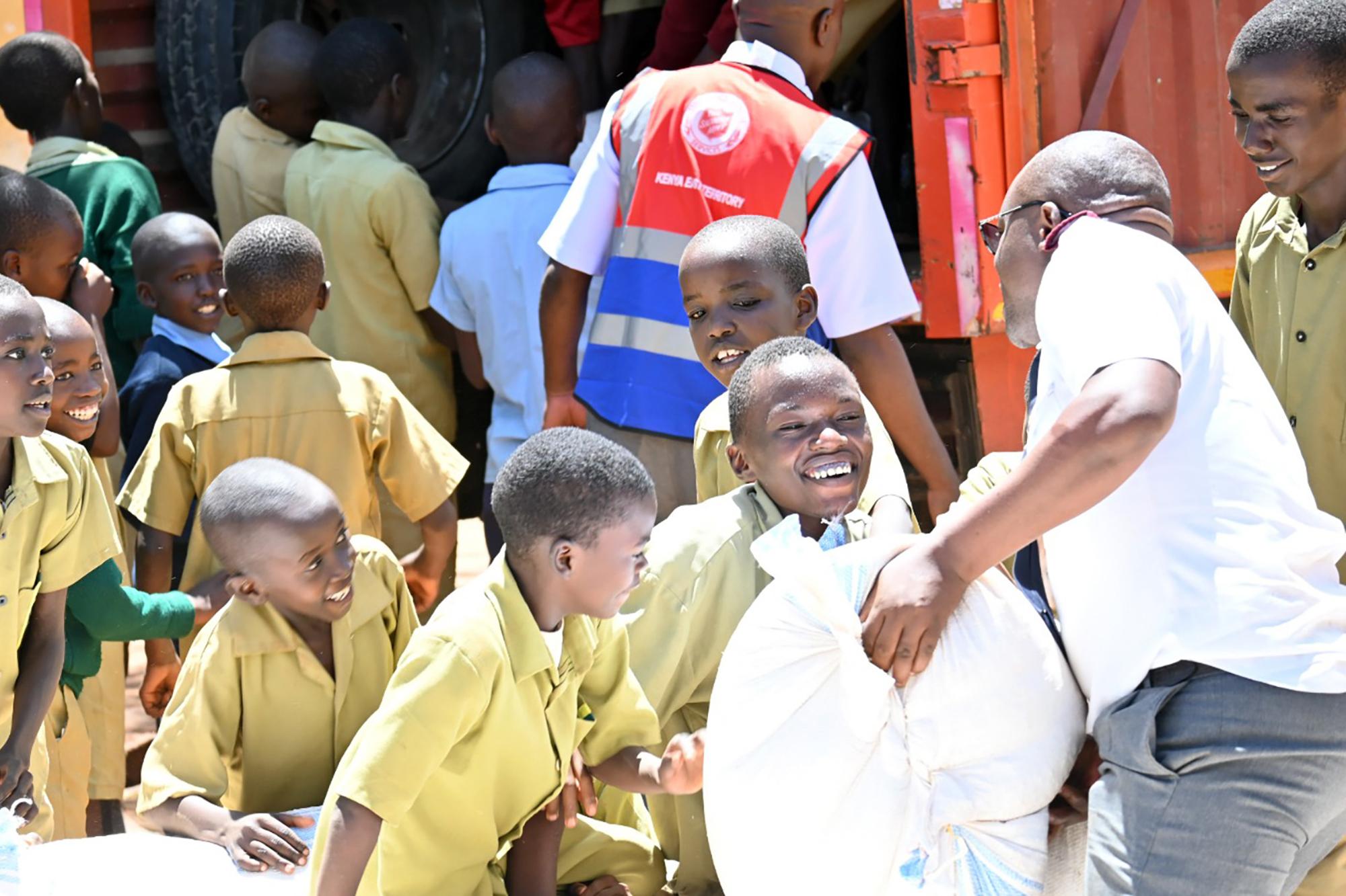 Ett gäng unga glada kenyanska pojkar hjälper till att ta emot säckar med majsmjöl från Frälsningsarméns personal.