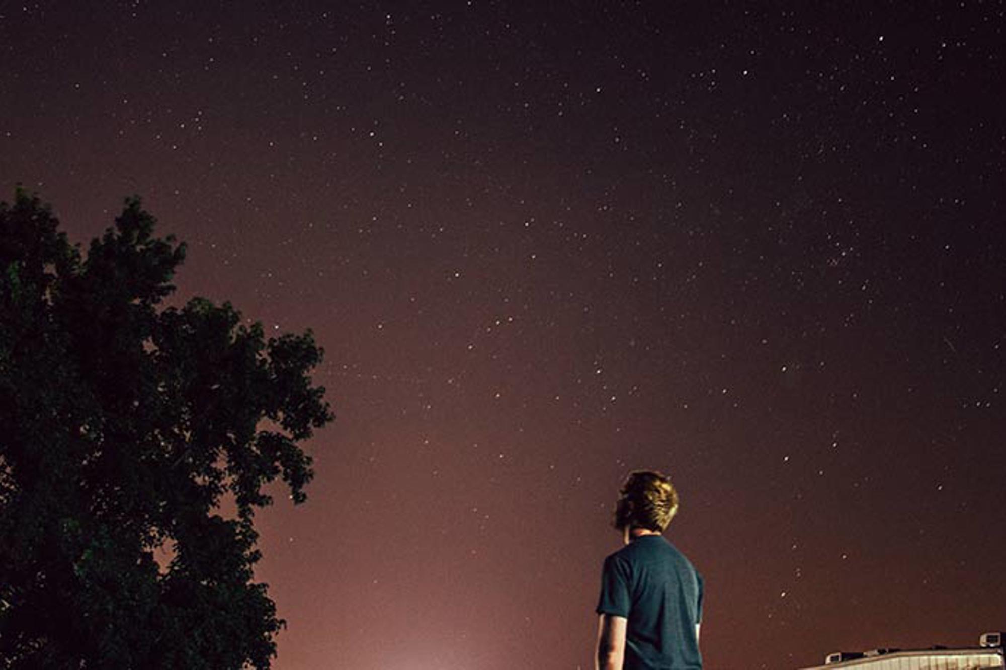Ryggtavlan på en man som står och tittar upp på en himmel full av stjärnor.
