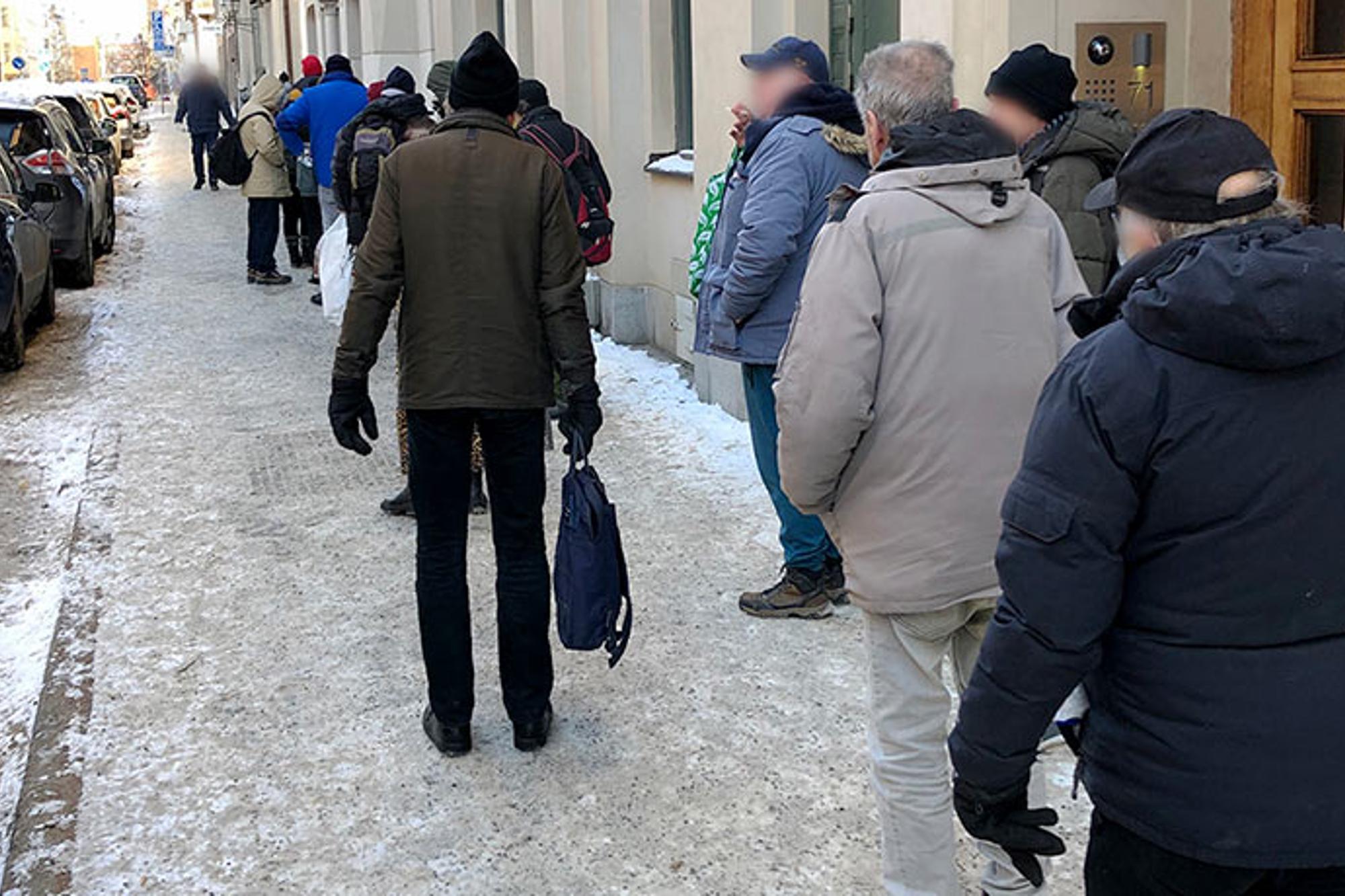 En lång kö av hjälpsökande som står längs med en gata utanför Templet i Stockholm. Personerna i kön står med ryggtavlorna mot kameran.