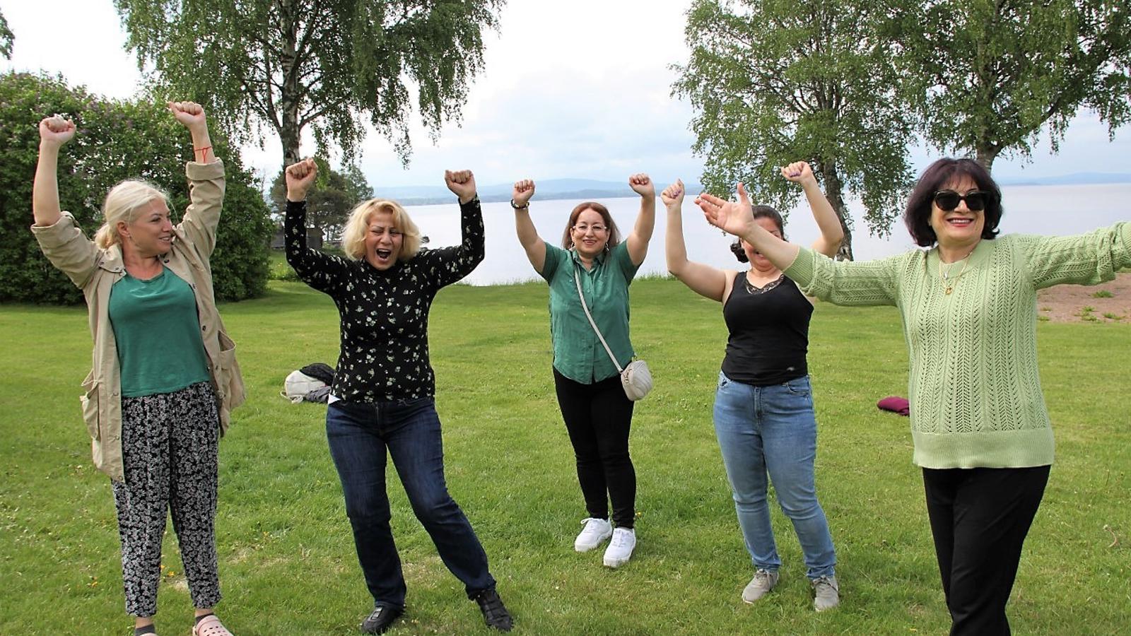 Fem glada kvinnor som står med armarna i luften utomhus i naturen.