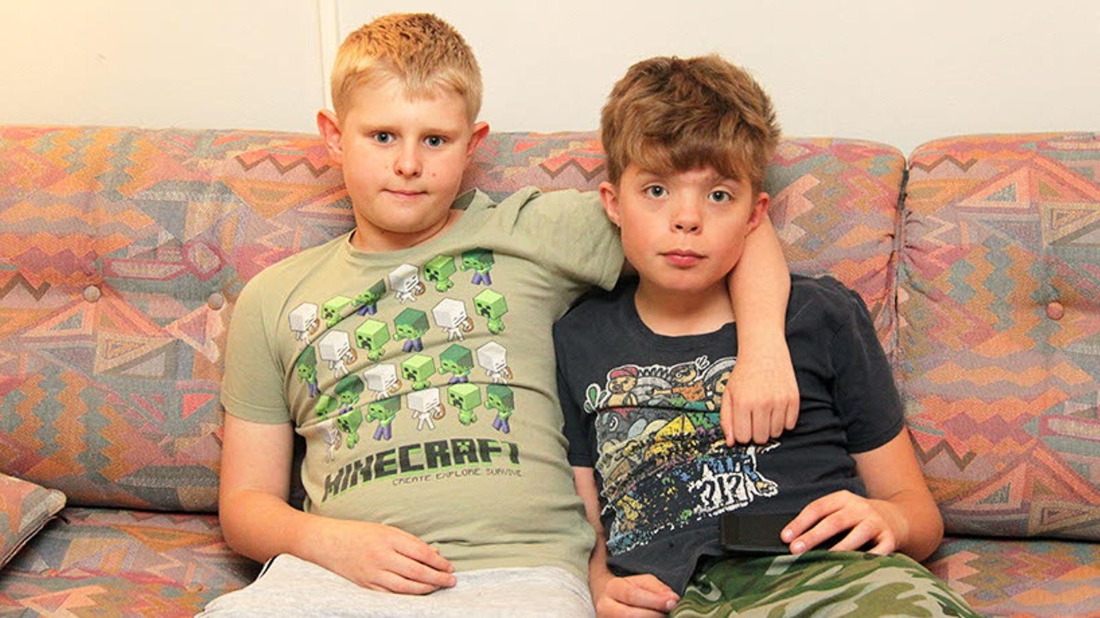 Två pojkar som sitter i en soffa och tittar in i kameran. Den ena pojken har armen runt den andra.