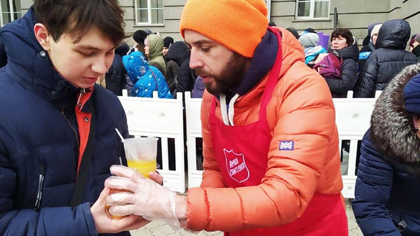 En man från Frälsningsarmén som delar ut mat och dryck till en kille i Ukraina.