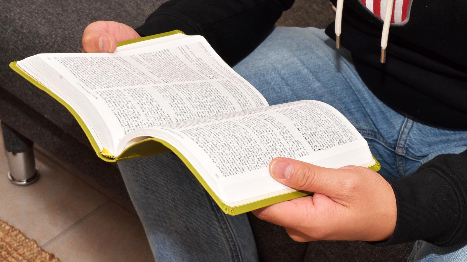 En uppslagen bibel i händerna och knät på en person klädd i jeans.